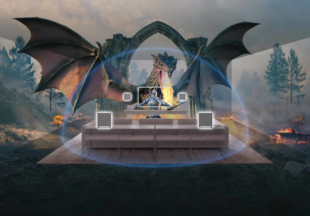 W pokoju znajduje się zestaw kina domowego z czterema głośnikami i telewizorem, na którym wyświetlany jest obraz smoka. W tle widoczne są drzewa i płomienie, tworzące scenerię fantasy.