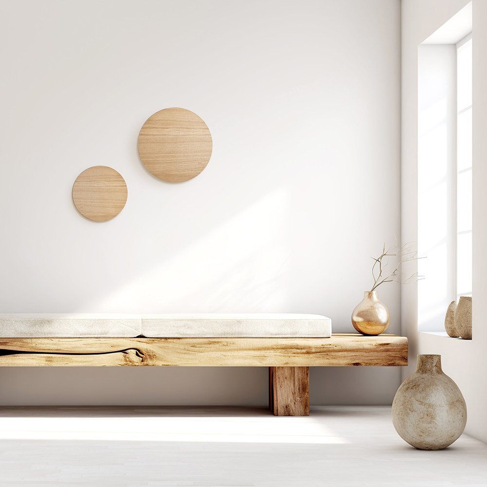 Minimalistyczne wnętrze z drewnianą ławką i dwoma okrągłymi dekoracjami na ścianie. Na ławce stoi wazon z gałązką, a na podłodze większy, ceramiczny wazon.