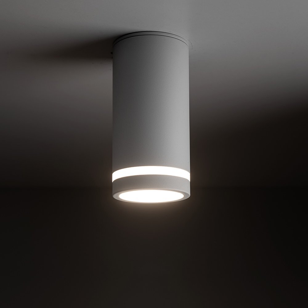 Biały, cylindryczny spot natynkowy zamontowany na suficie, emitujący jasne światło. Wykonany z metalu, ma nowoczesny design z widocznym pierścieniem świetlnym.