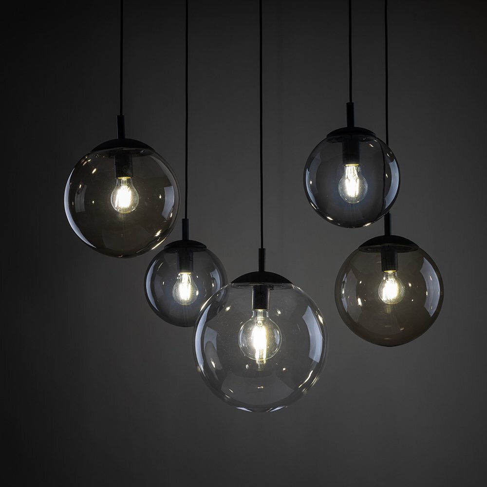 Na ciemnym tle widać pięć wiszących lamp z przezroczystymi, kulistymi kloszami, w których znajdują się żarówki emitujące jasne światło. Lampy są zawieszone na czarnych przewodach.