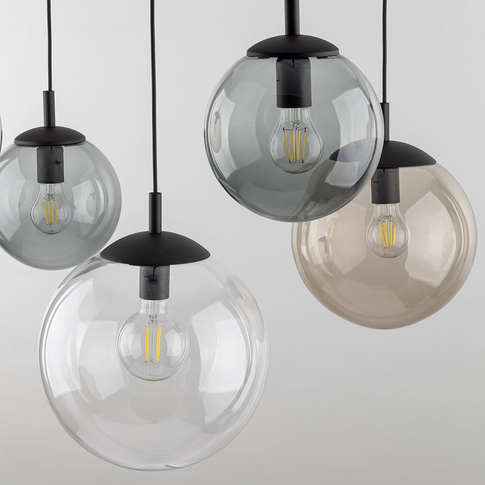 Na obrazie widoczne są cztery szklane klosze lamp wiszących w różnych odcieniach szarości i brązu, z widocznymi żarówkami wewnątrz. Klosze są zawieszone na czarnych przewodach.