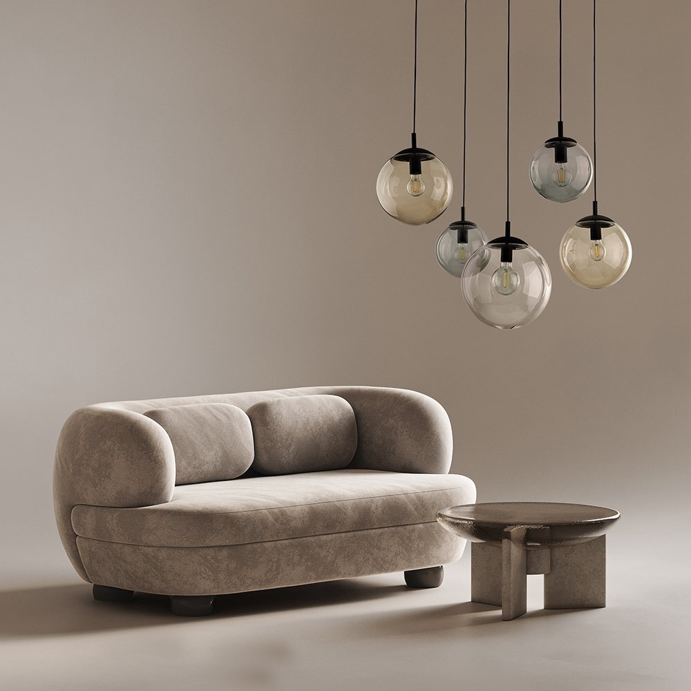 Na obrazie widoczna jest nowoczesna lampa wisząca z pięcioma szklanymi kloszami w różnych kolorach. W tle znajduje się beżowa sofa i okrągły stolik.