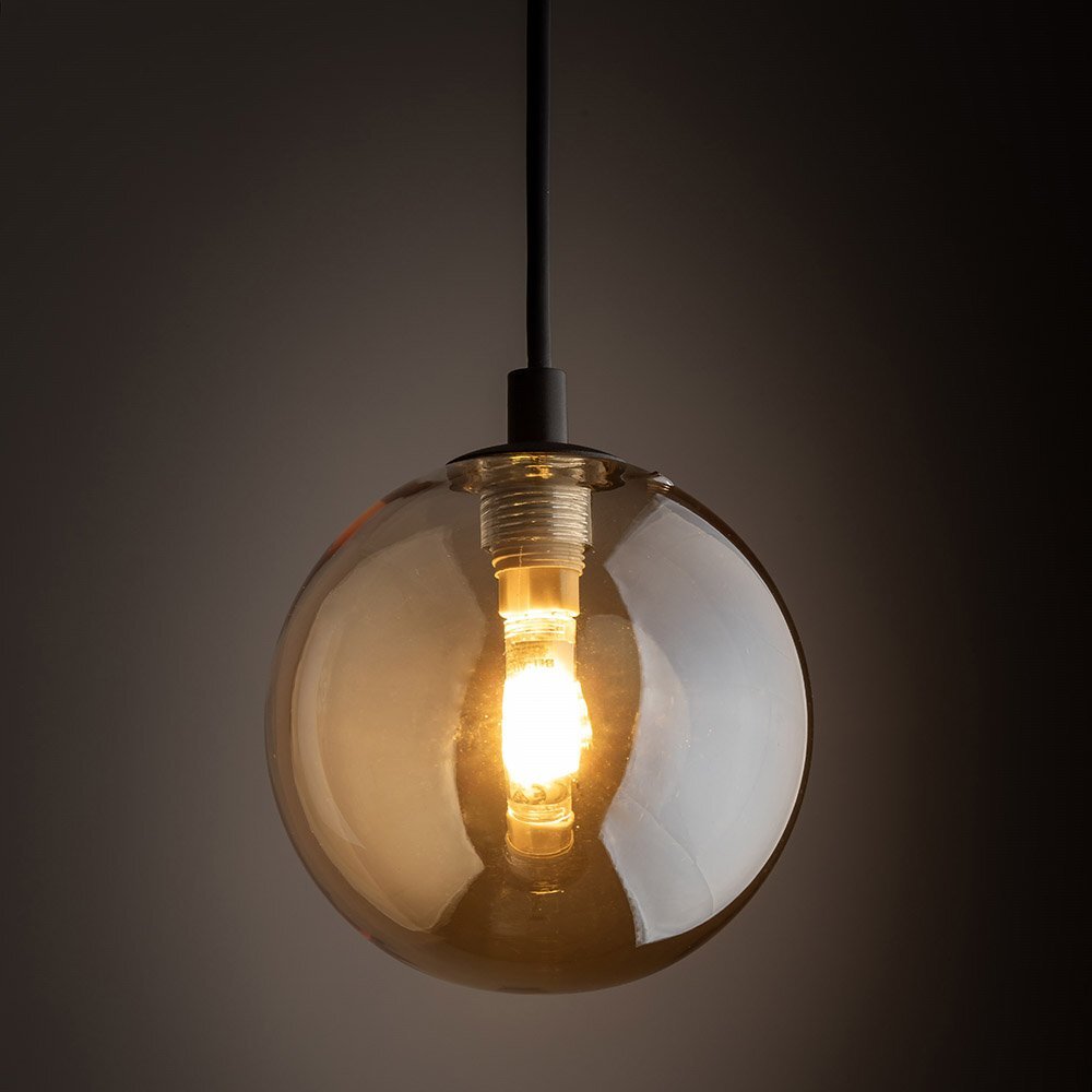 Lampa wisząca z bursztynowym szklanym kloszem, emitująca ciepłe światło. Klosz ma kulisty kształt, a lampa jest zawieszona na czarnym przewodzie.