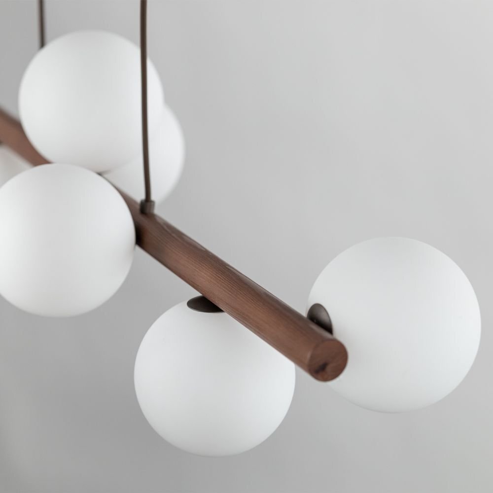 Lampa wisząca z drewnianym elementem w kolorze orzecha, posiadająca kilka białych, kulistych kloszy. Klosze są rozmieszczone symetrycznie wokół drewnianej belki.