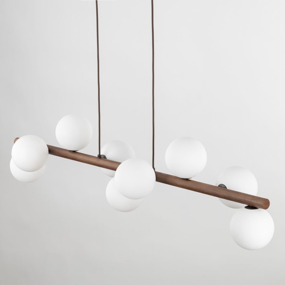Lampa wisząca z drewnianym elementem w kolorze orzecha, wyposażona w dziewięć białych, kulistych kloszy. Lampa jest zawieszona na dwóch ciemnych przewodach, umożliwiających regulację wysokości.