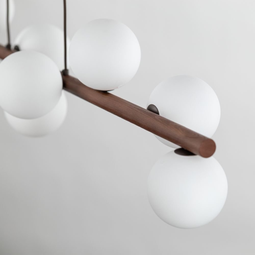 Lampa wisząca z białymi, kulistymi kloszami zamocowanymi na drewnianej belce w kolorze orzecha. Klosze są równomiernie rozmieszczone wzdłuż belki.