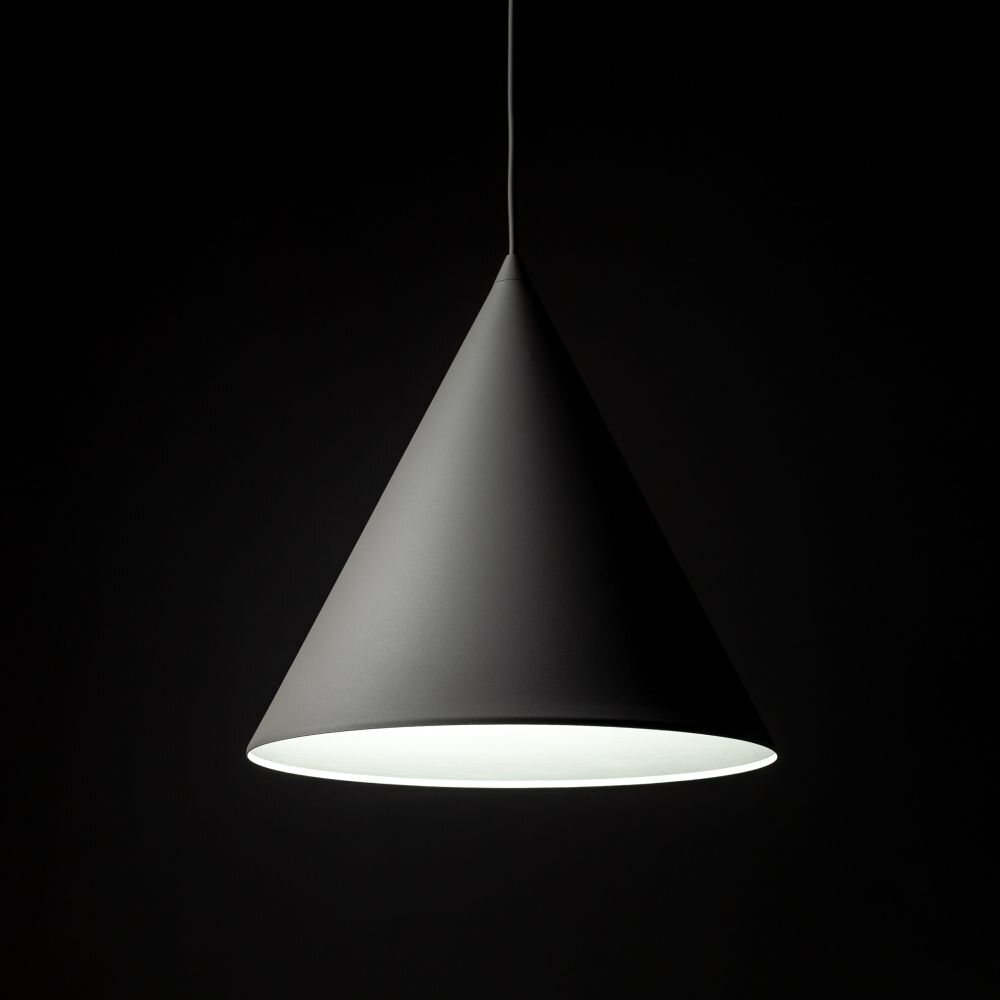 Na obrazie widoczna jest wisząca lampa w kształcie stożka, o gładkiej powierzchni i ciemnym kolorze. Tło jest jednolicie czarne, co podkreśla kształt lampy.