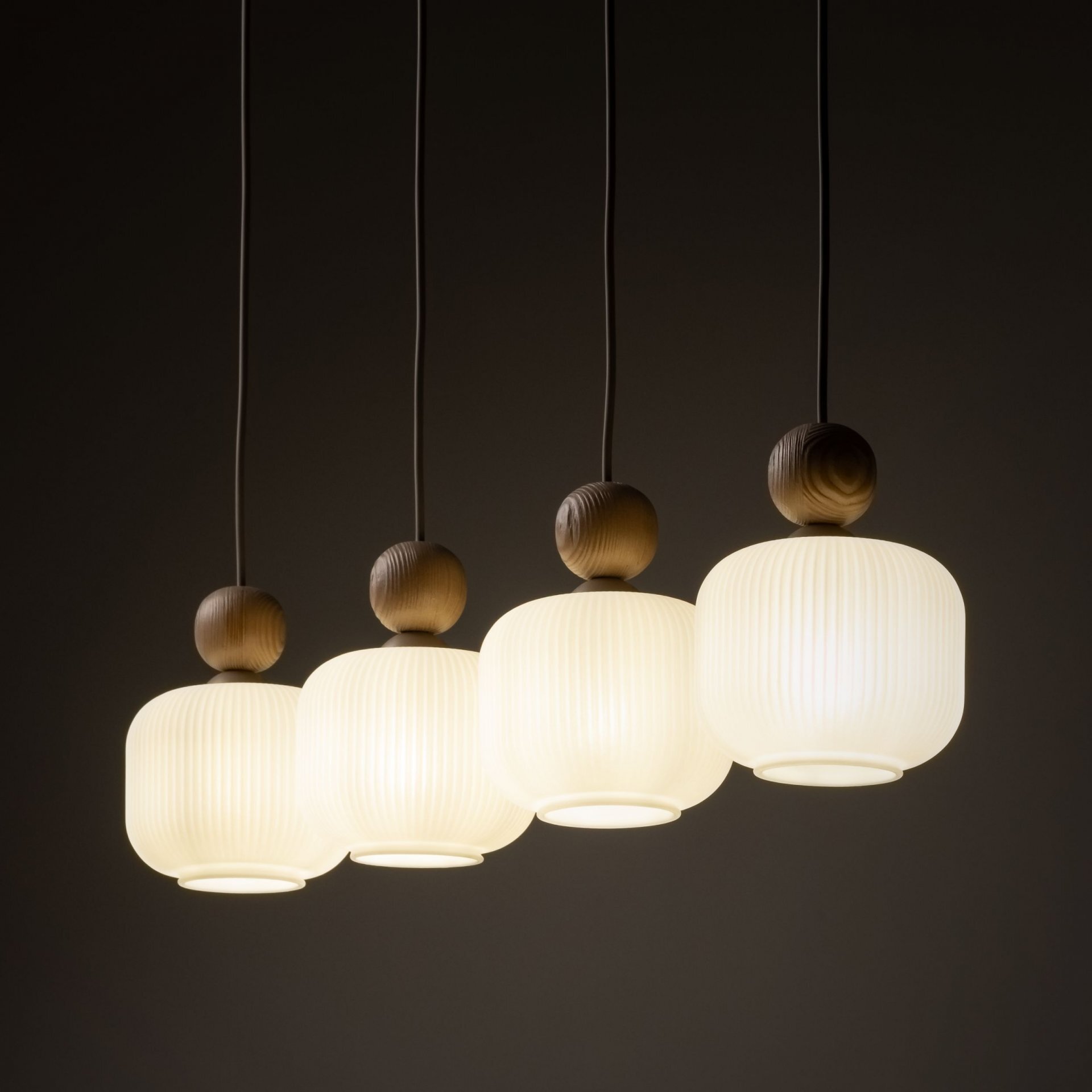 Cztery wiszące lampy z białymi, szklanymi kloszami o żebrowanej fakturze, zawieszone na ciemnych przewodach. Każda lampa ma drewniany element nad kloszem.