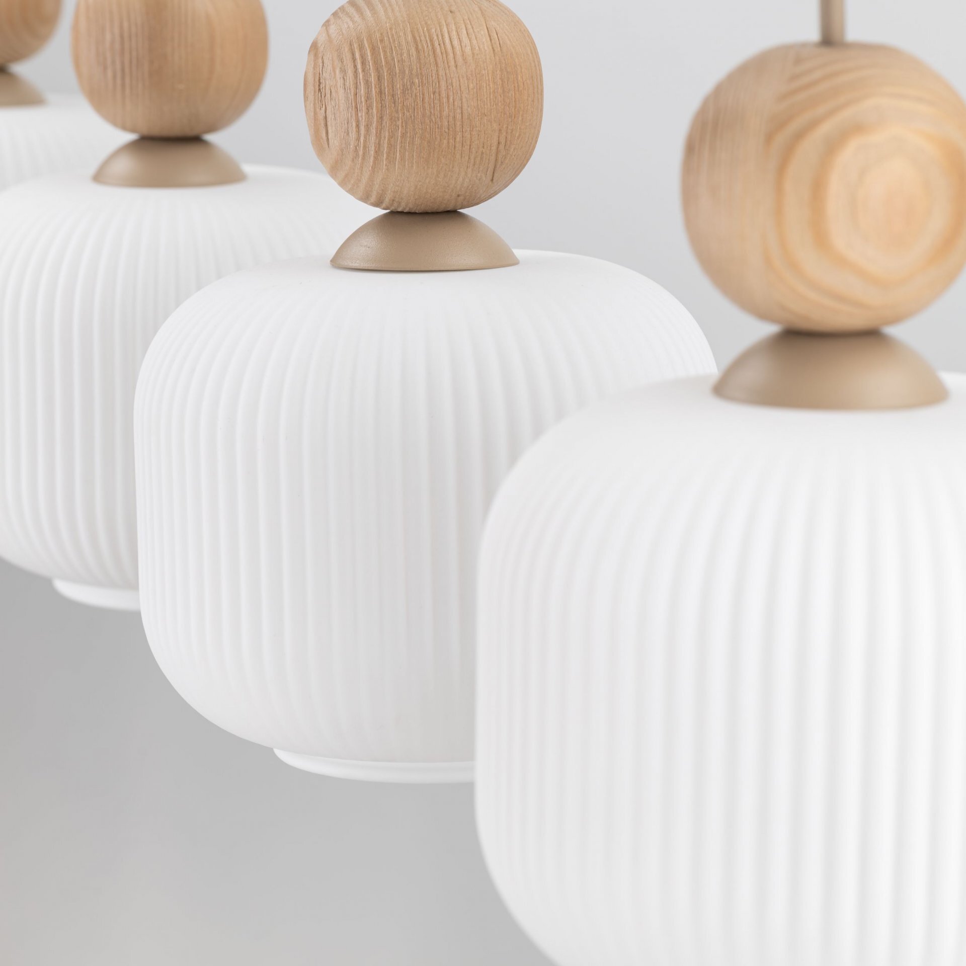 Na obrazie widoczne są cztery białe, żebrowane klosze lamp wiszących z drewnianymi kulami na górze. Klosze są wykonane z metalu i szkła.
