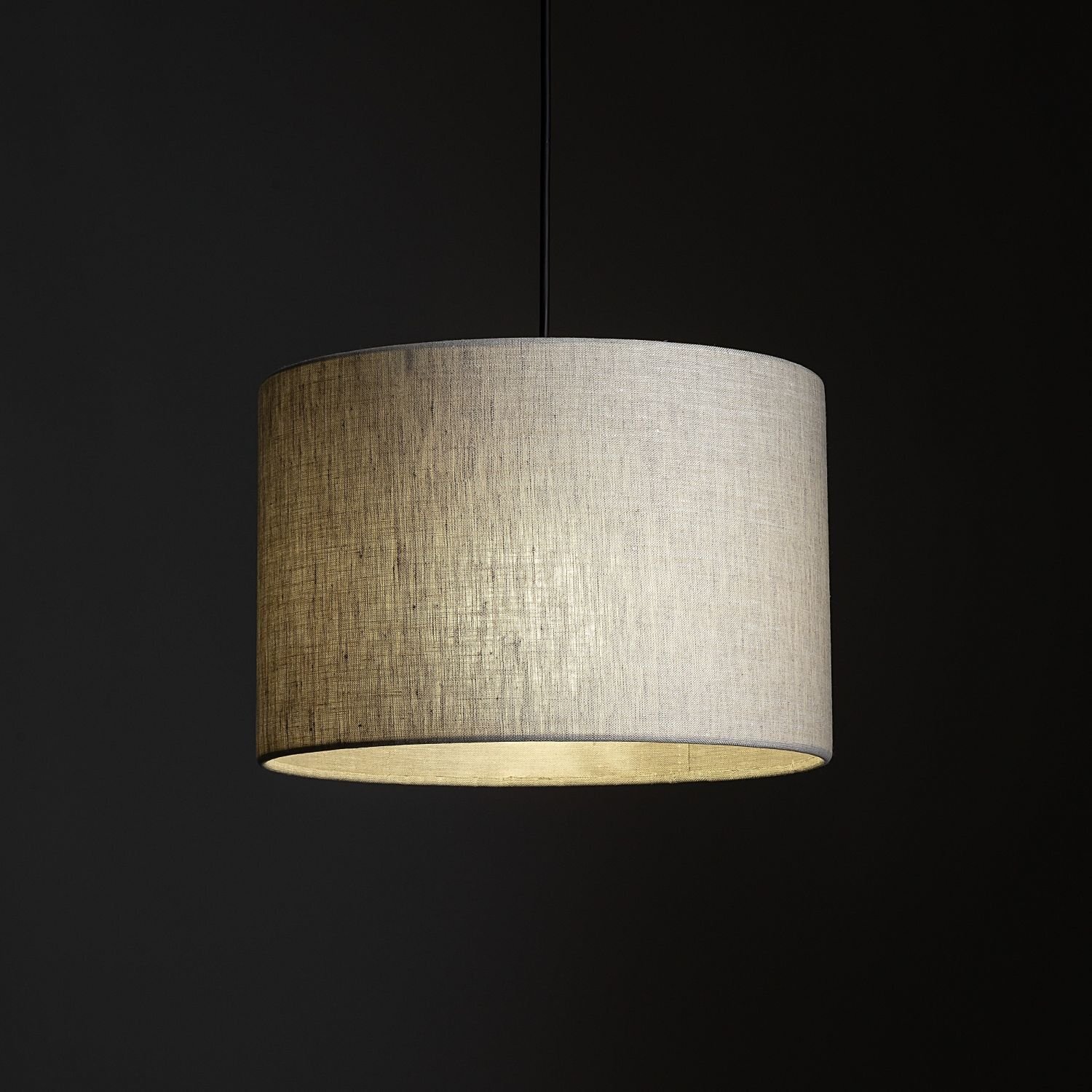 Lampa wisząca z cylindrycznym abażurem w kolorze beżowym, zawieszona na czarnym przewodzie. Tło jest ciemne, co podkreśla jasny kolor abażuru.