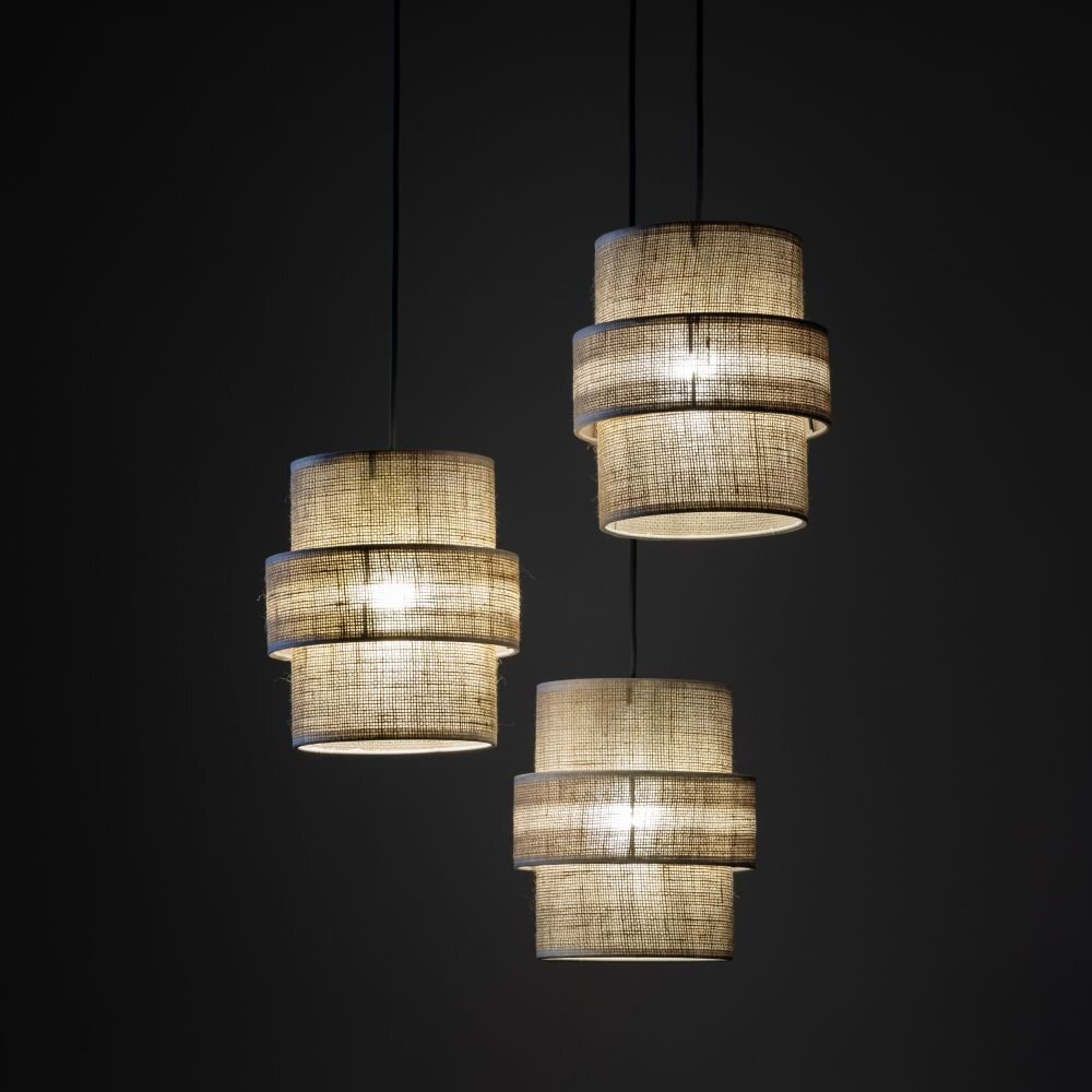 Trzy wiszące lampy z czarno-jutowymi abażurami, każda o cylindrycznym kształcie i widocznym źródle światła wewnątrz. Lampy zawieszone są na ciemnym tle, co podkreśla ich nowoczesny design.