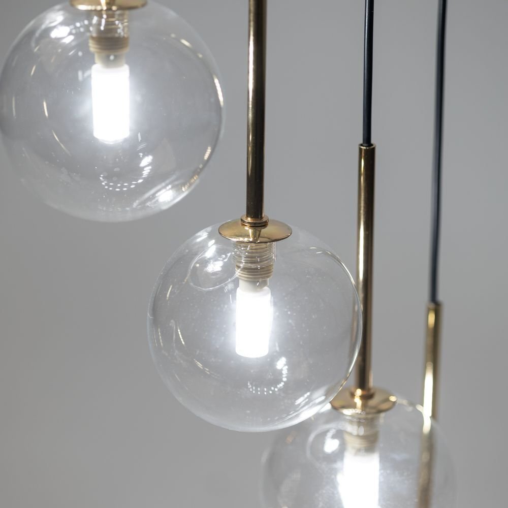 Na zdjęciu widoczne są trzy szklane klosze lamp wiszących z żarówkami, zamocowane na czarno-złotych uchwytach. Klosze są przezroczyste, a światło żarówek jest białe i intensywne.