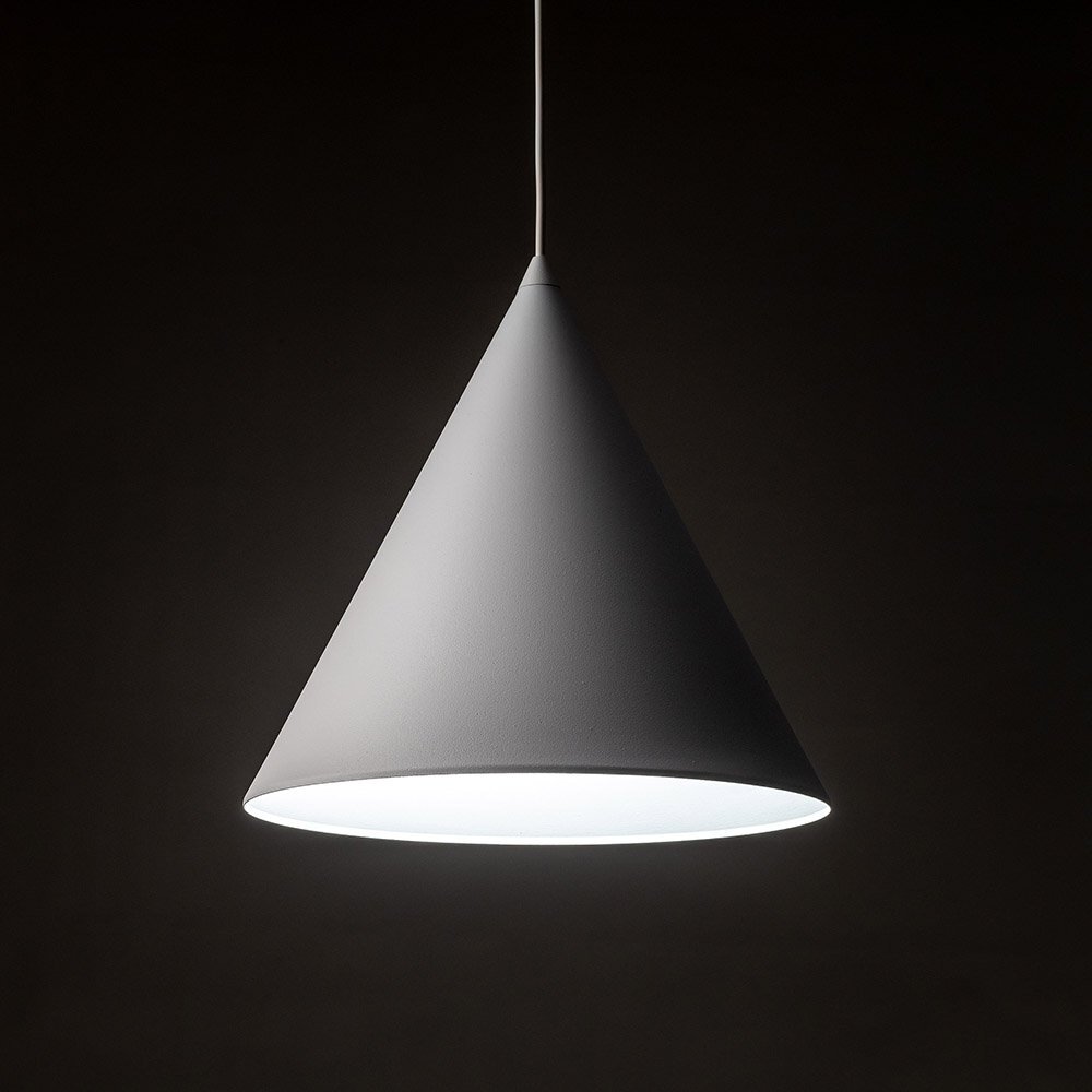 Na obrazie widoczna jest biała, stożkowa lampa wisząca z metalowym kloszem. Lampa jest zawieszona na cienkim przewodzie, a jej wnętrze jest oświetlone.