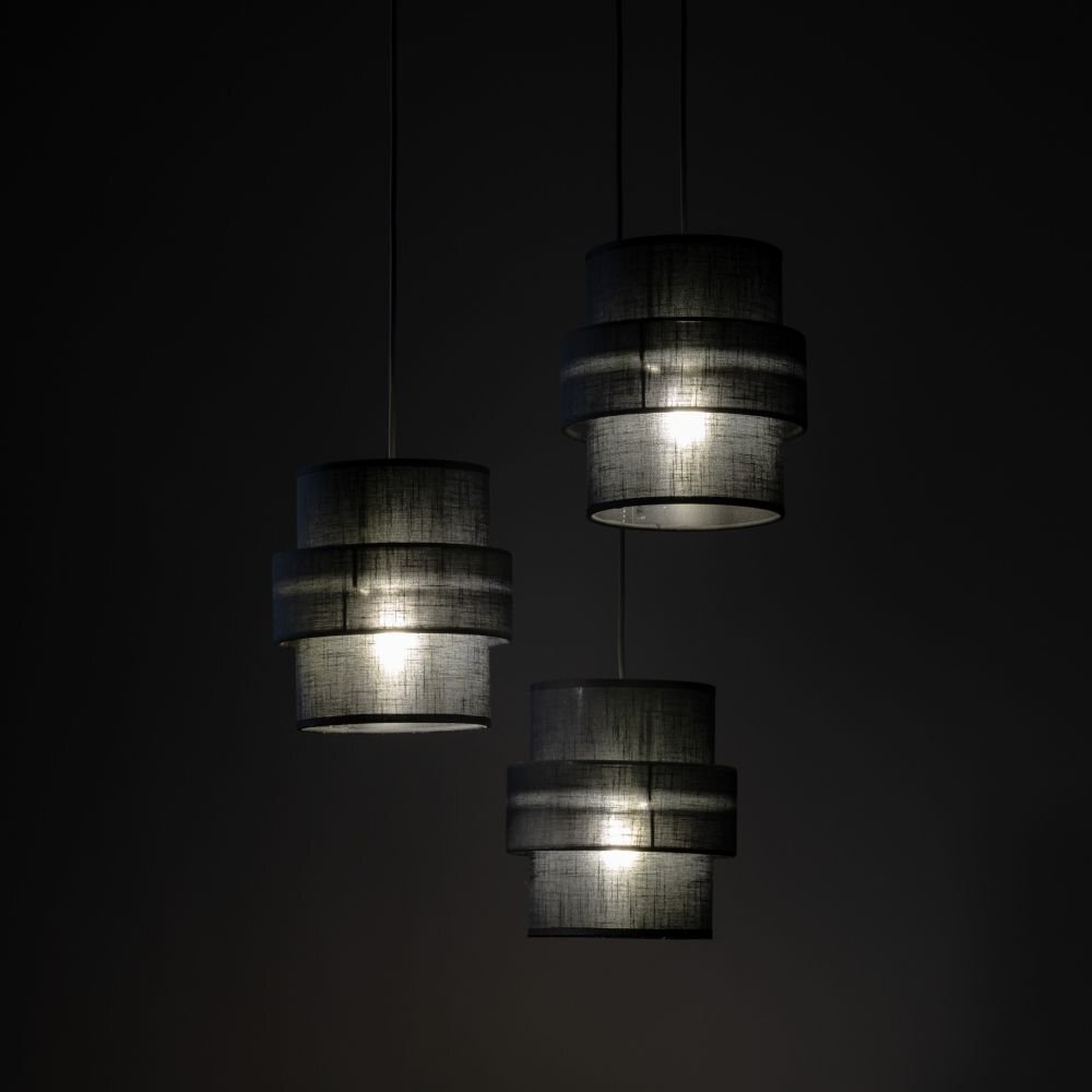 Trzy czarne, wiszące lampy z cylindrycznymi abażurami, emitujące miękkie światło. Lampy zawieszone są na cienkich przewodach na ciemnym tle.