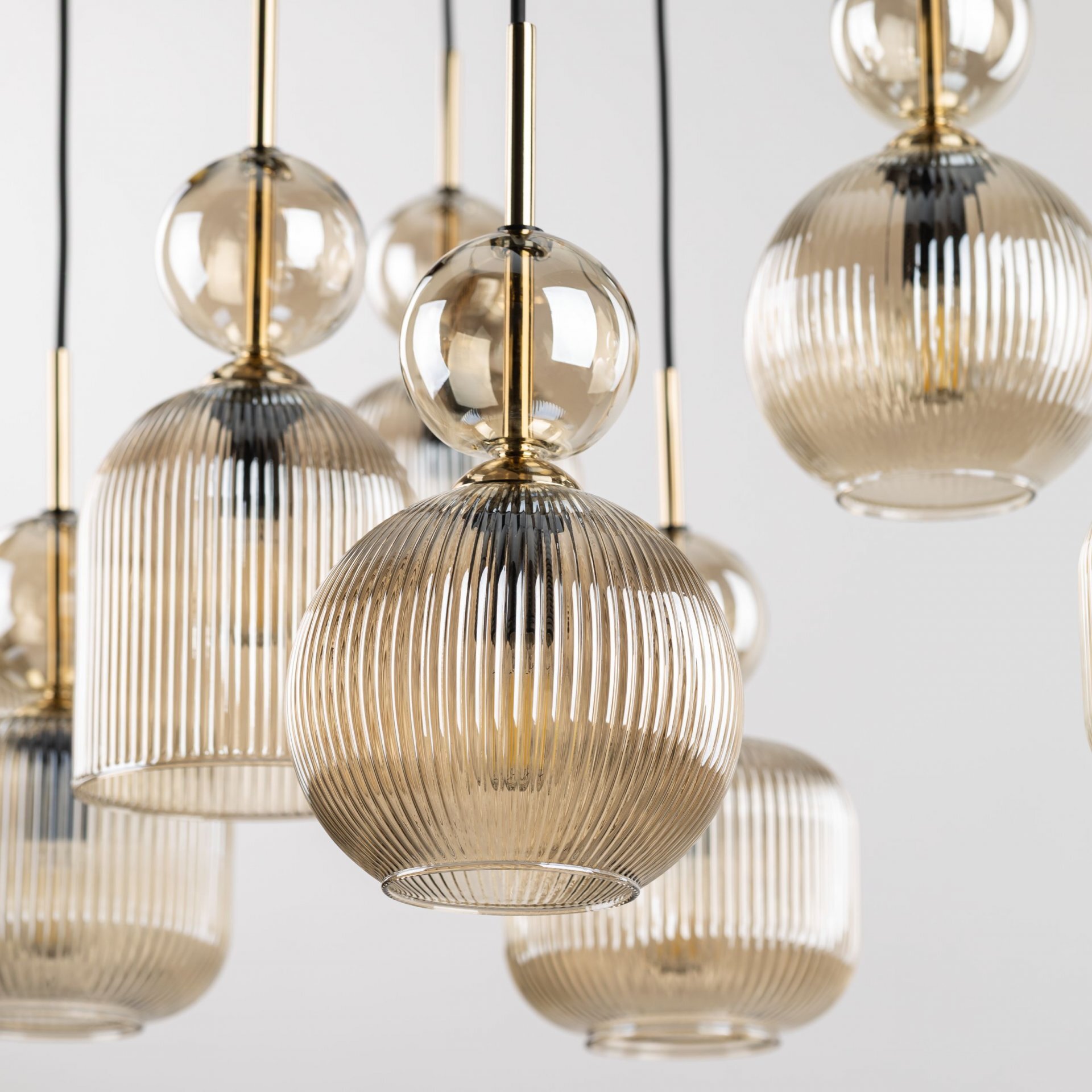 Zdjęcie przedstawia kilka szklanych kloszy lamp wiszących w kolorze koniakowym, z wyraźnym żłobieniem i złotymi elementami mocującymi. Klosze mają kulisty kształt i są zawieszone na czarnych przewodach.