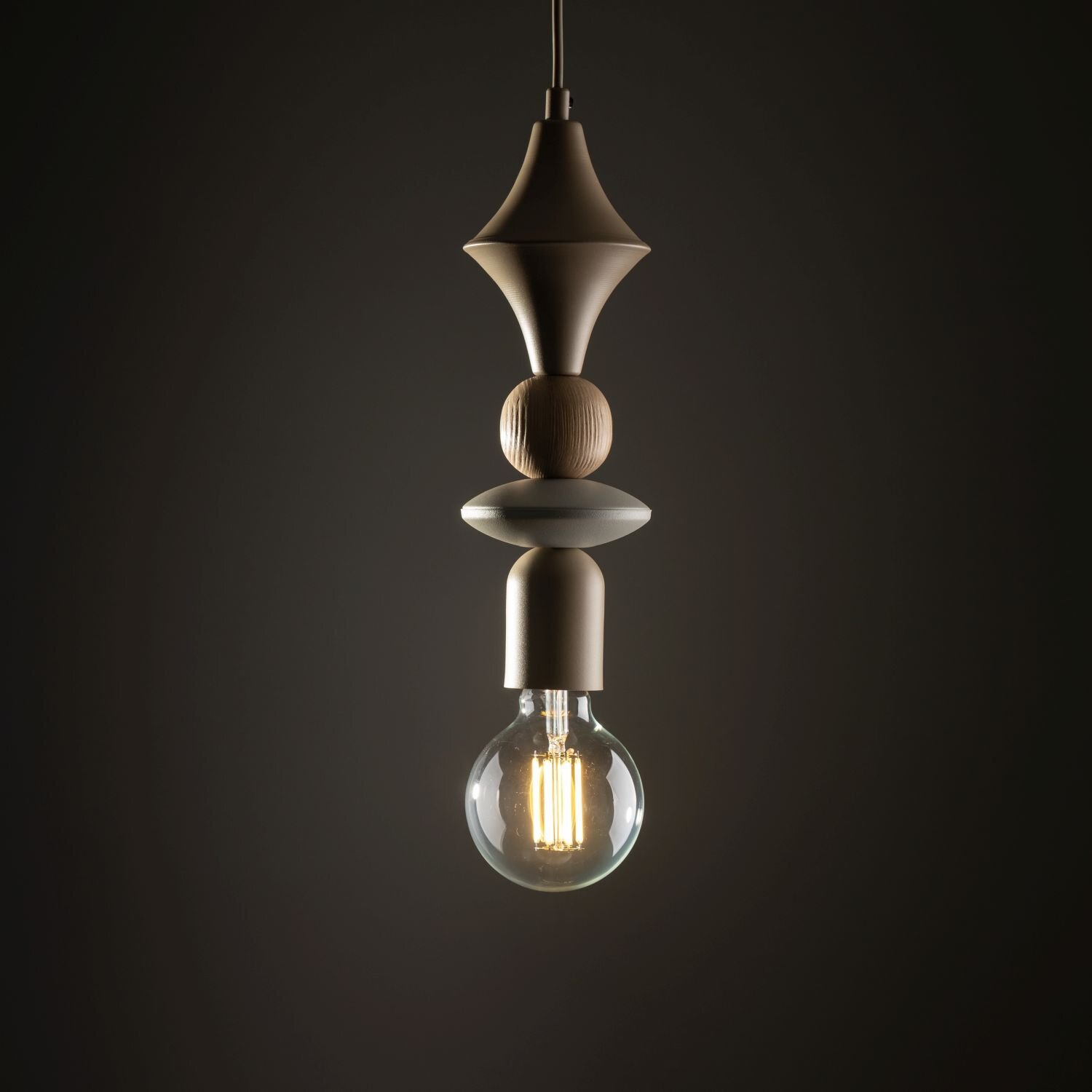Lampa wisząca z beżowym kloszem w kształcie cylindra, z widoczną żarówką E27. Elementy dekoracyjne w różnych kształtach i odcieniach beżu, zawieszone na ciemnym tle.