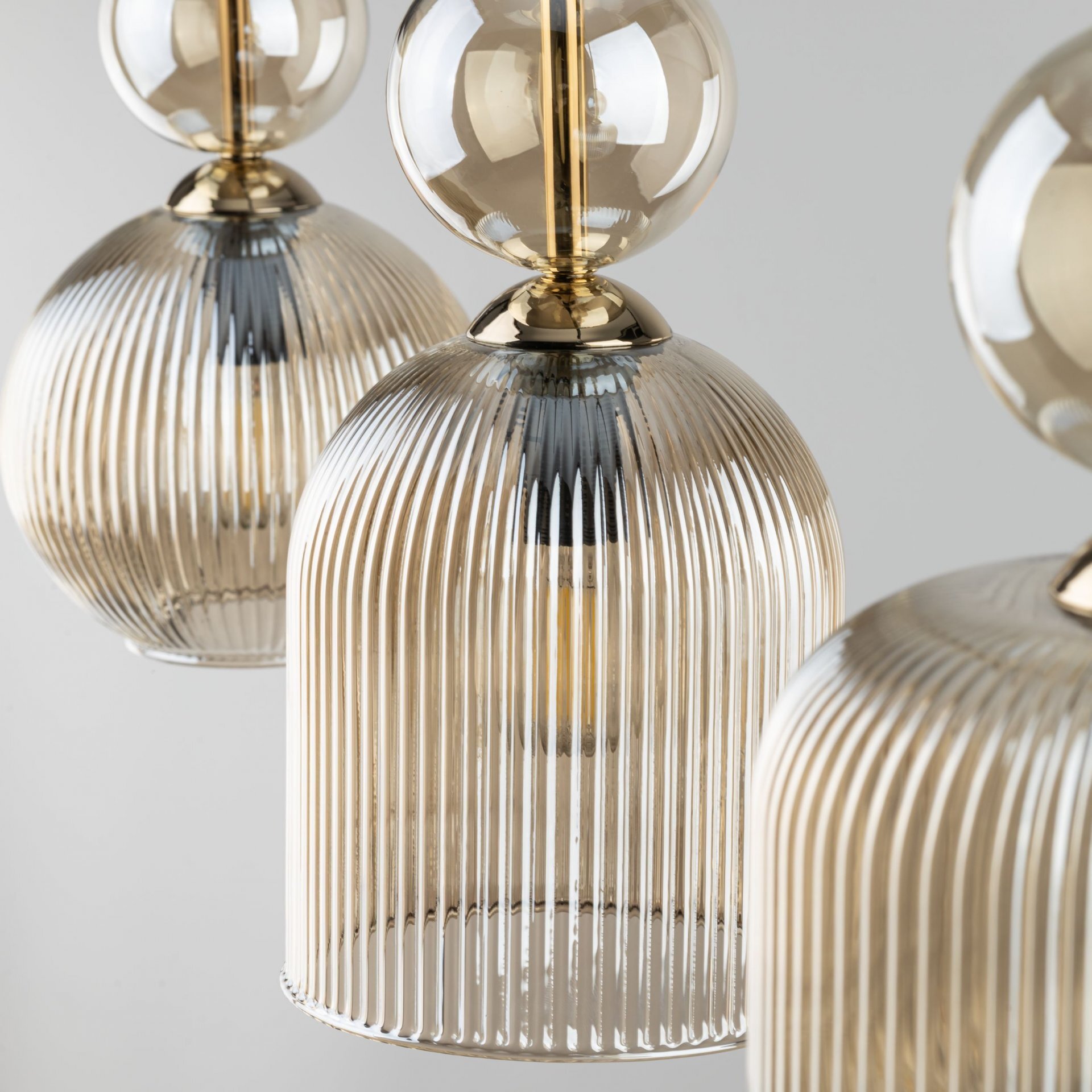 Zdjęcie przedstawia trzy wiszące lampy z bursztynowymi kloszami o żebrowanej strukturze. Elementy metalowe lamp są w kolorze złotym.