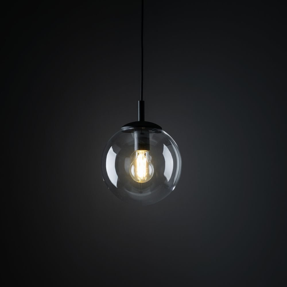 Na ciemnym tle wisi lampa z przezroczystym, kulistym kloszem, wewnątrz którego znajduje się żarówka emitująca ciepłe światło.