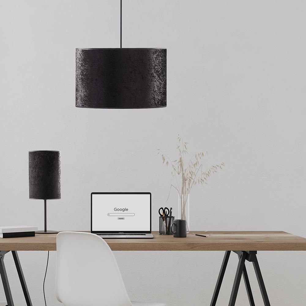 Na obrazie widoczna jest czarna lampa wisząca o cylindrycznym kształcie, zawieszona nad biurkiem. Na biurku znajduje się laptop z widoczną stroną Google, obok którego stoją przybory biurowe i wazon z suchymi gałązkami.
