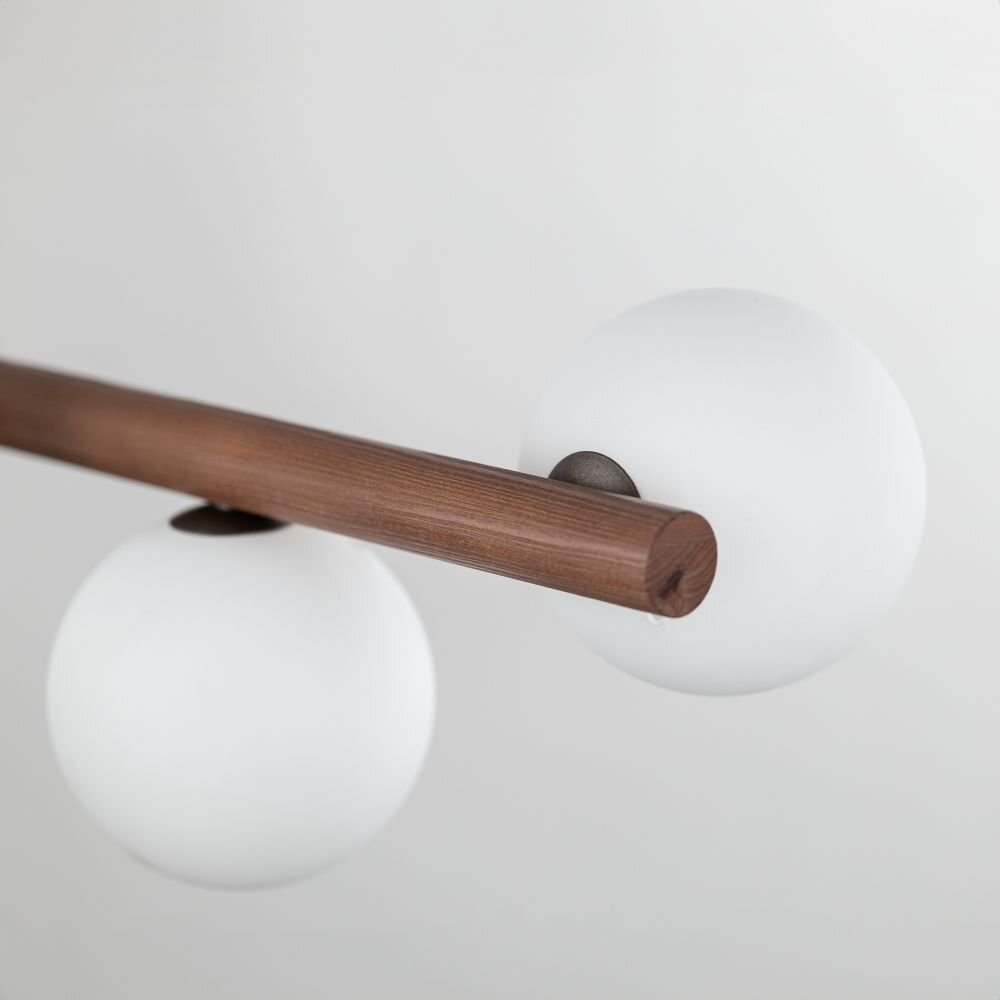 Na obrazie widoczna jest lampa wisząca z drewnianym elementem w kolorze orzecha i białymi, kulistymi kloszami. Lampa ma nowoczesny design i jest przeznaczona do wnętrz takich jak jadalnia, kuchnia czy salon.