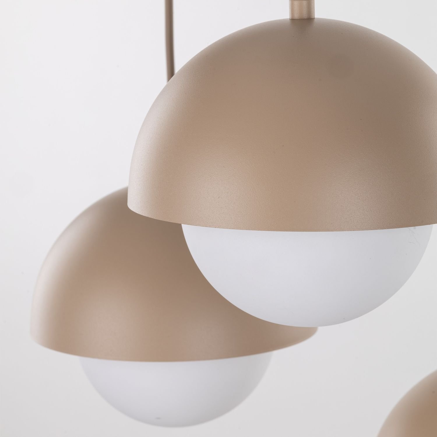 Na obrazie widoczne są dwie beżowe lampy wiszące o półkulistym kształcie z białymi kloszami. Lampy mają gładką powierzchnię i są zawieszone na przewodach.