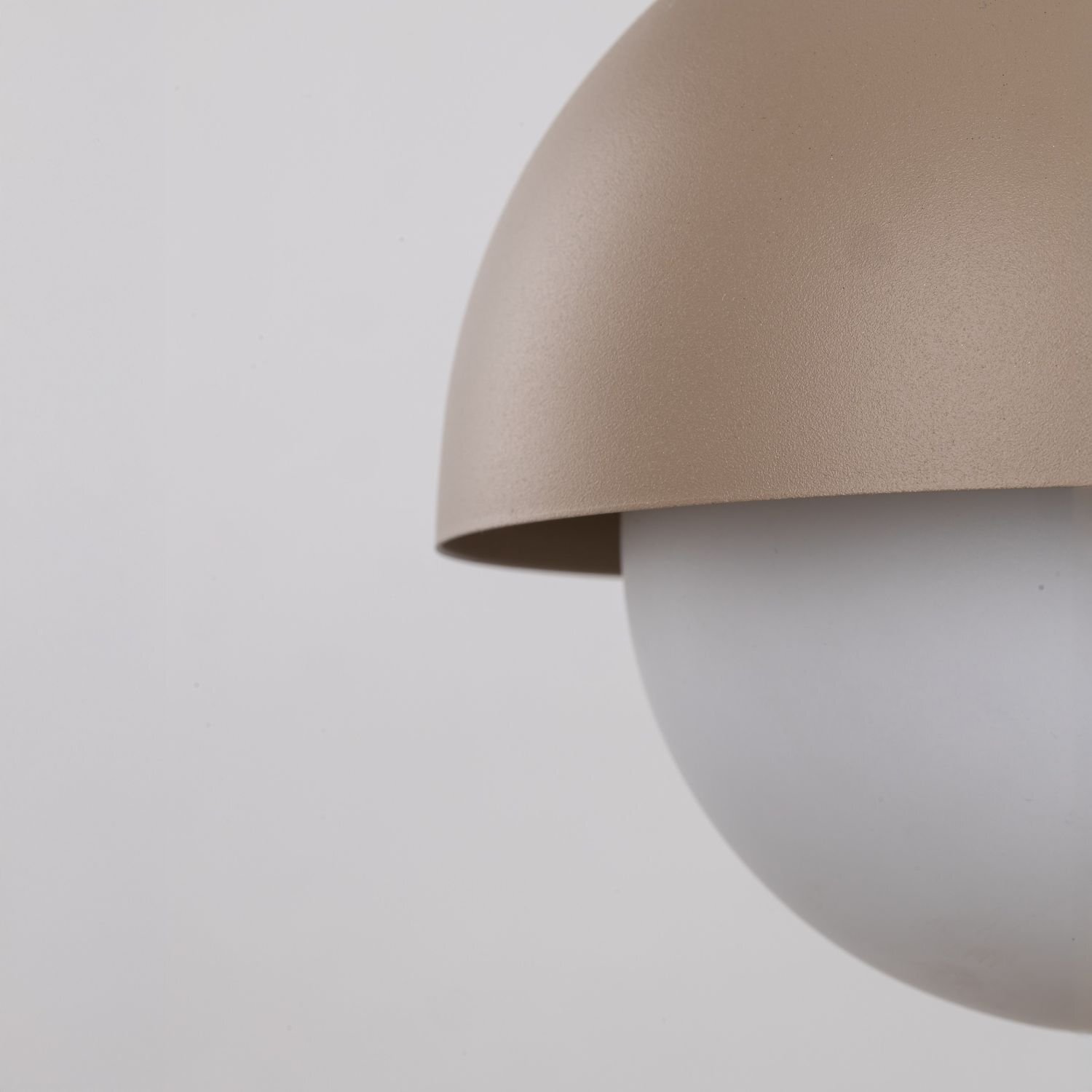 Zbliżenie na beżowy klosz lampy wiszącej z białą, matową kulą. Lampa ma gładką powierzchnię i minimalistyczny design.