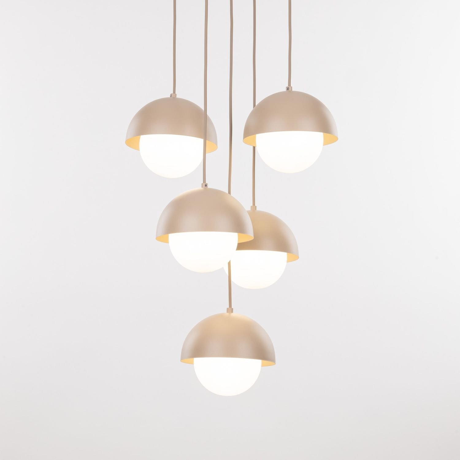 Na obrazie widoczna jest lampa wisząca z pięcioma kloszami w kształcie półkul, w kolorze beżowym. Klosze są zawieszone na przewodach, a ich dolna część jest biała i przepuszcza światło.