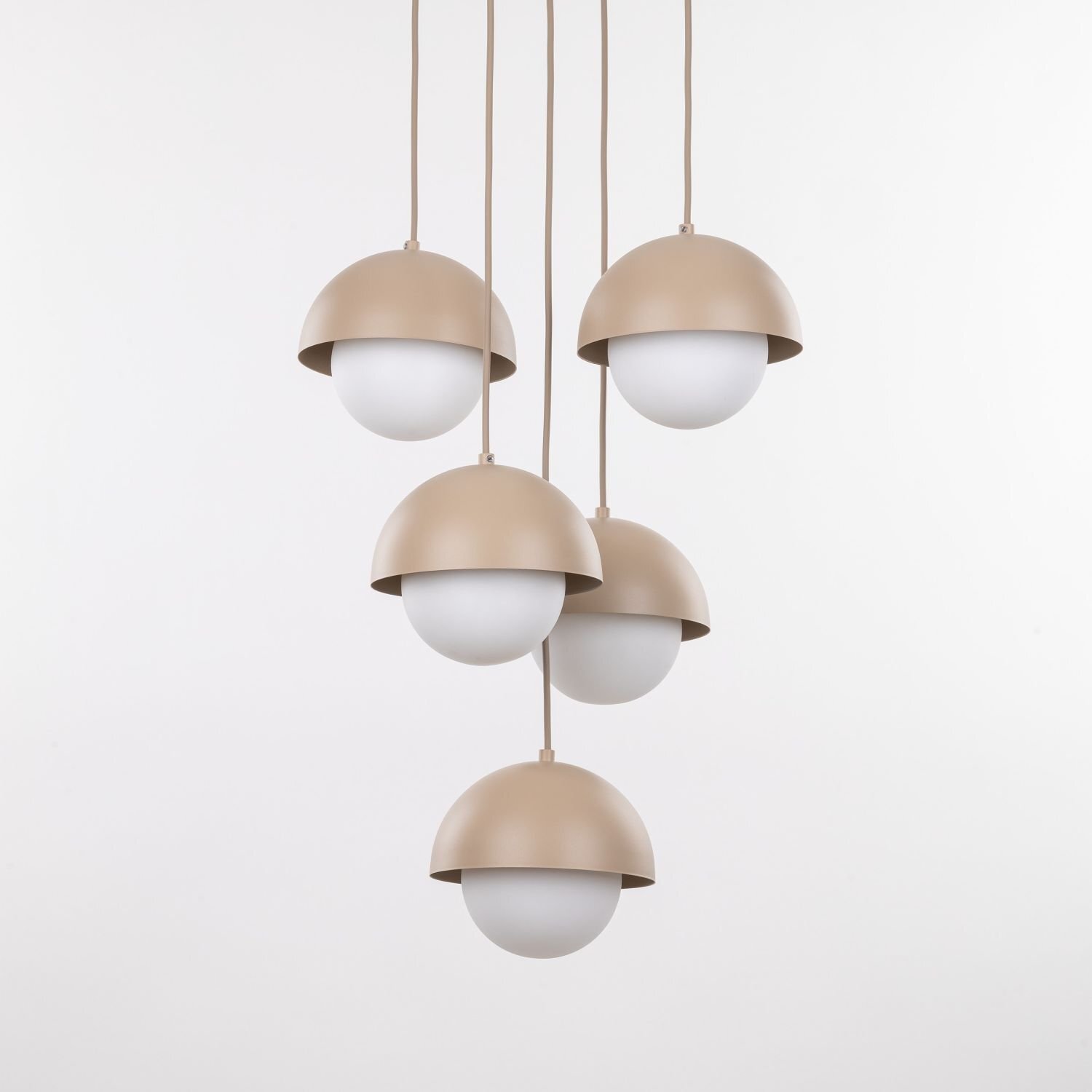 Na obrazie widoczna jest lampa wisząca z pięcioma kloszami w kształcie półkul, w kolorze beżowym i białym. Klosze są zawieszone na przewodach, a tło jest jednolite i jasne.