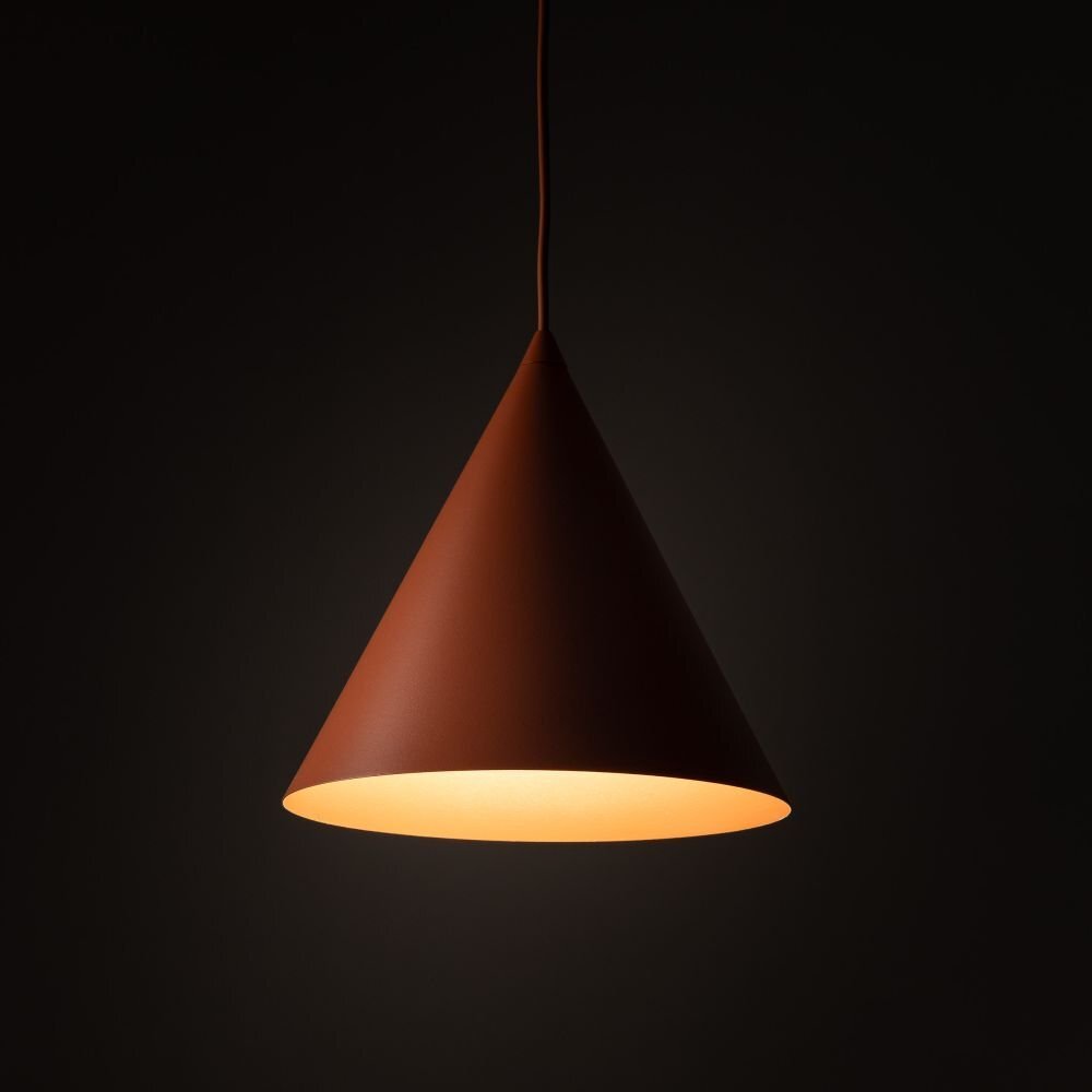Czerwona lampa wisząca o stożkowym kształcie, emitująca ciepłe światło. Tło jest ciemne, co podkreśla jasność lampy.