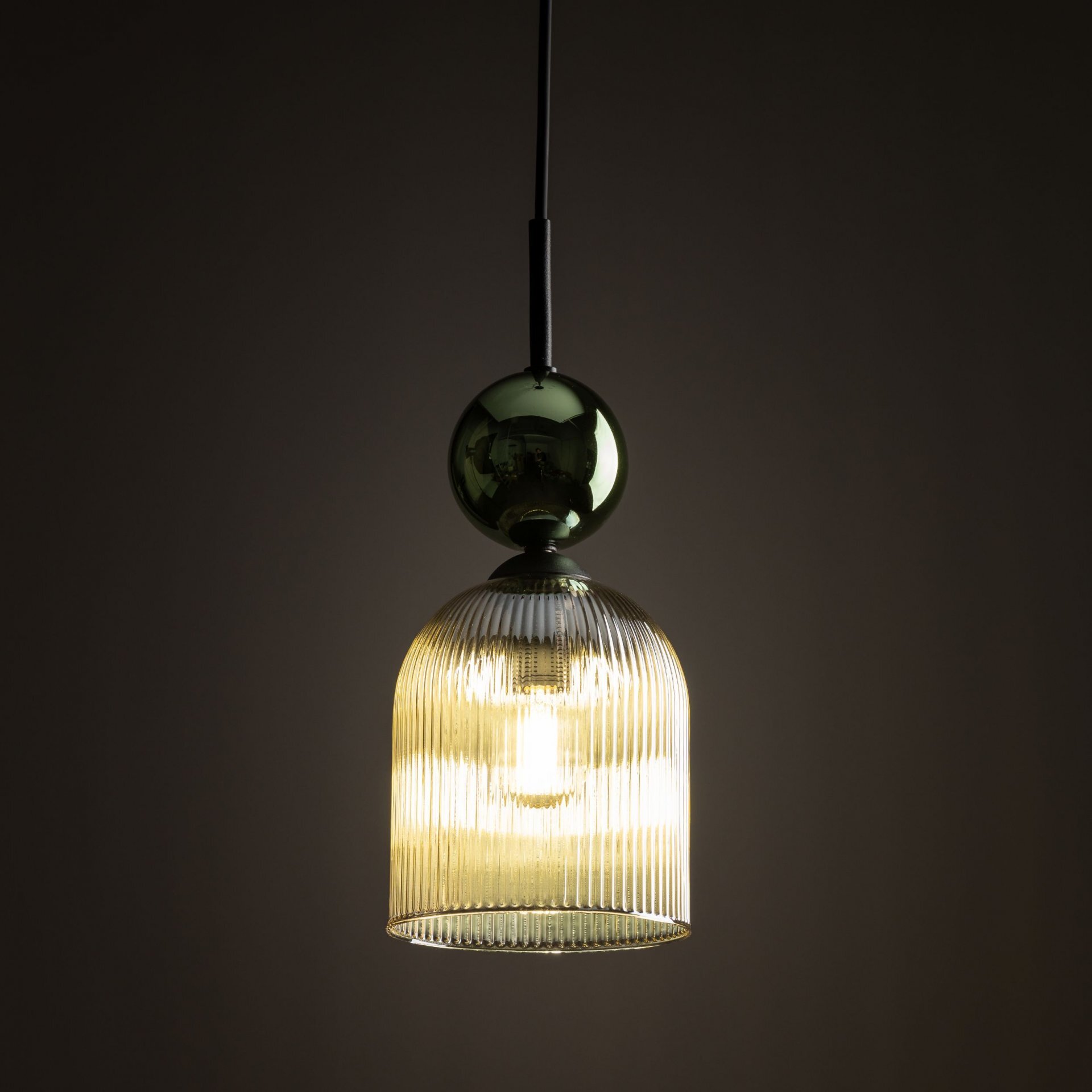 Lampa wisząca z żarówką wewnątrz, wykonana z zielono-bursztynowego szkła o żebrowanej strukturze. Górna część lampy ma kulisty kształt i ciemniejszy odcień.