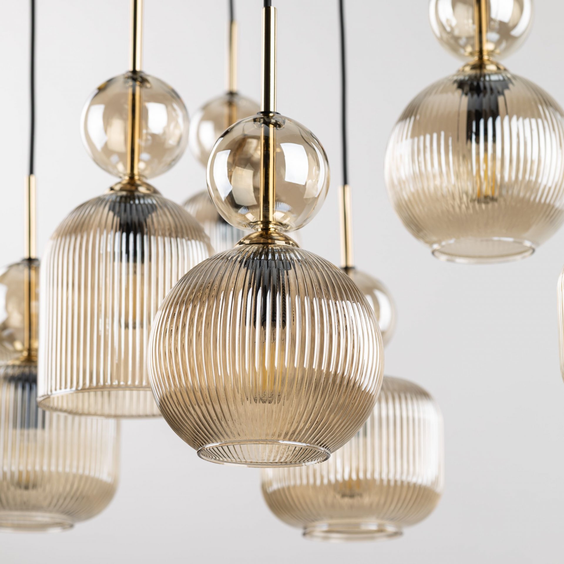 Zdjęcie przedstawia kilka wiszących lamp z żarówkami w szklanych, żłobionych kloszach o bursztynowym odcieniu. Elementy metalowe lamp są w kolorze złotym.