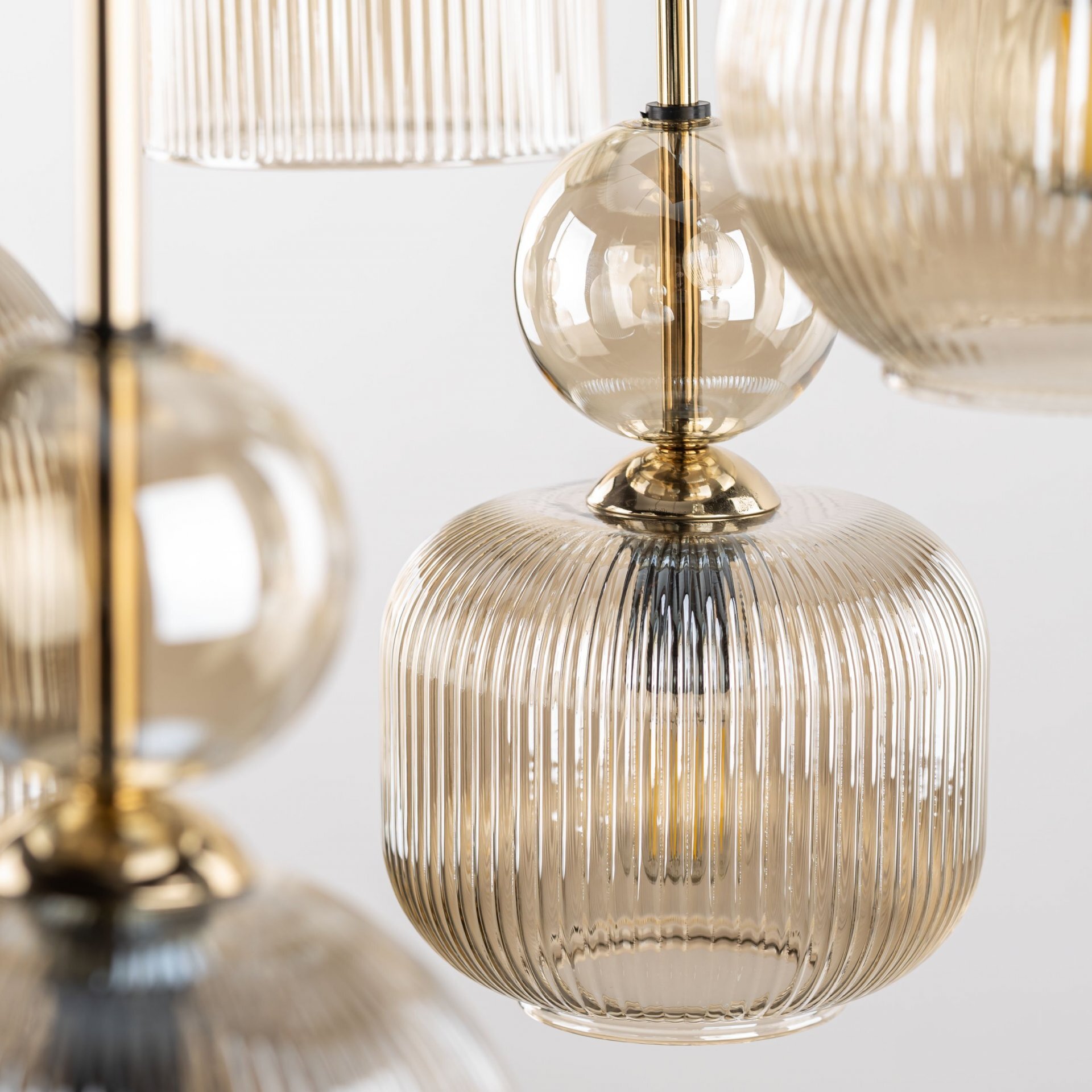 Zbliżenie na elementy lampy wiszącej z przezroczystego, żebrowanego szkła w kolorze bursztynowym z metalicznymi, złotymi detalami. Lampa ma elegancki, nowoczesny design.