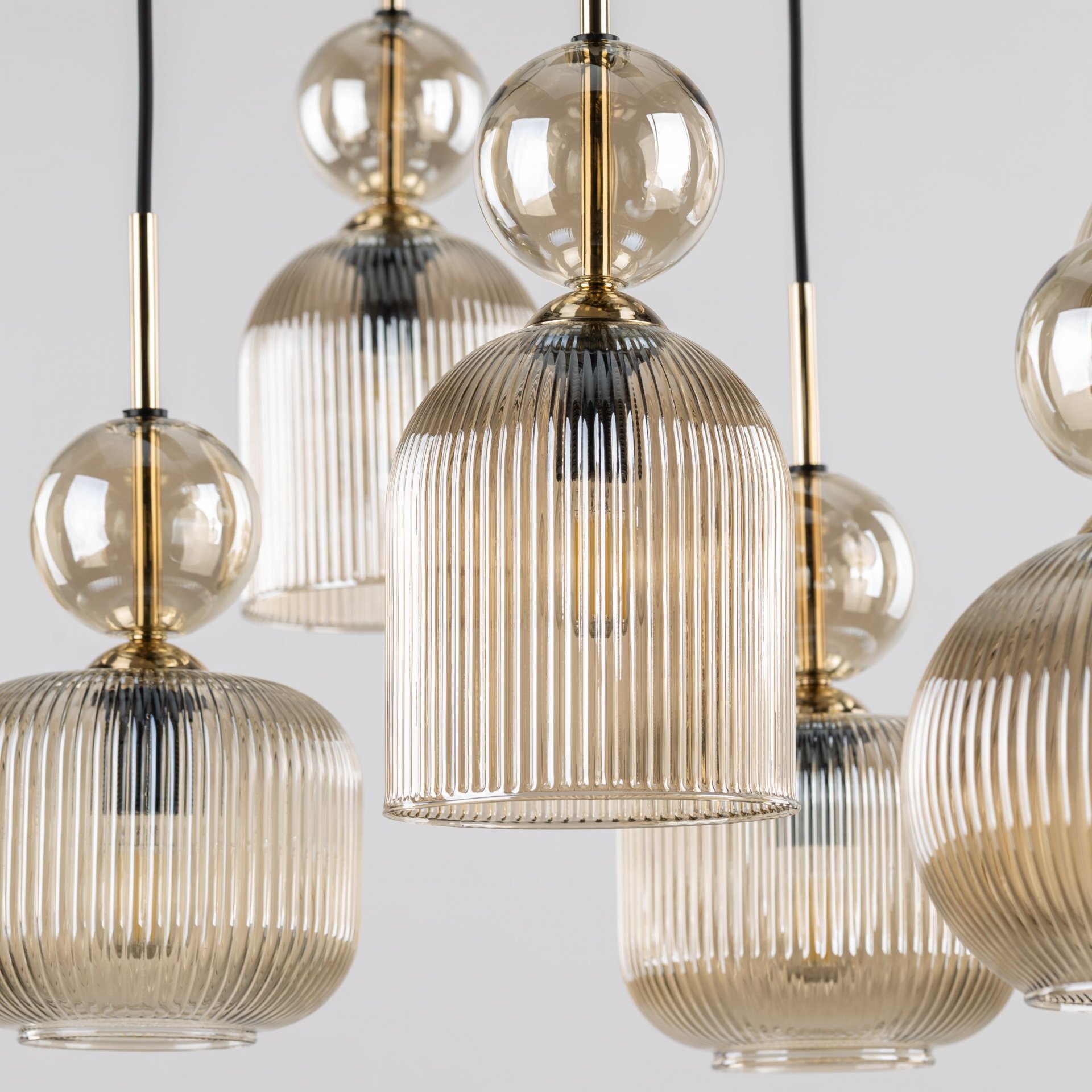 Zdjęcie przedstawia kilka wiszących lamp z żarówkami w przezroczystych, żłobionych kloszach w kolorze bursztynowym. Elementy metalowe lamp są w kolorze złotym.
