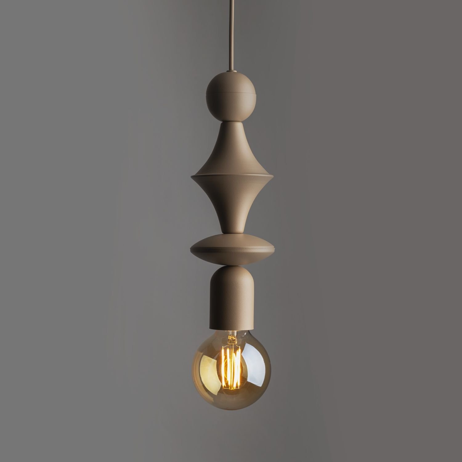 Beżowa lampa wisząca o nowoczesnym designie z metalowym korpusem i widoczną żarówką. Tło jest jednolite i ciemnoszare.
