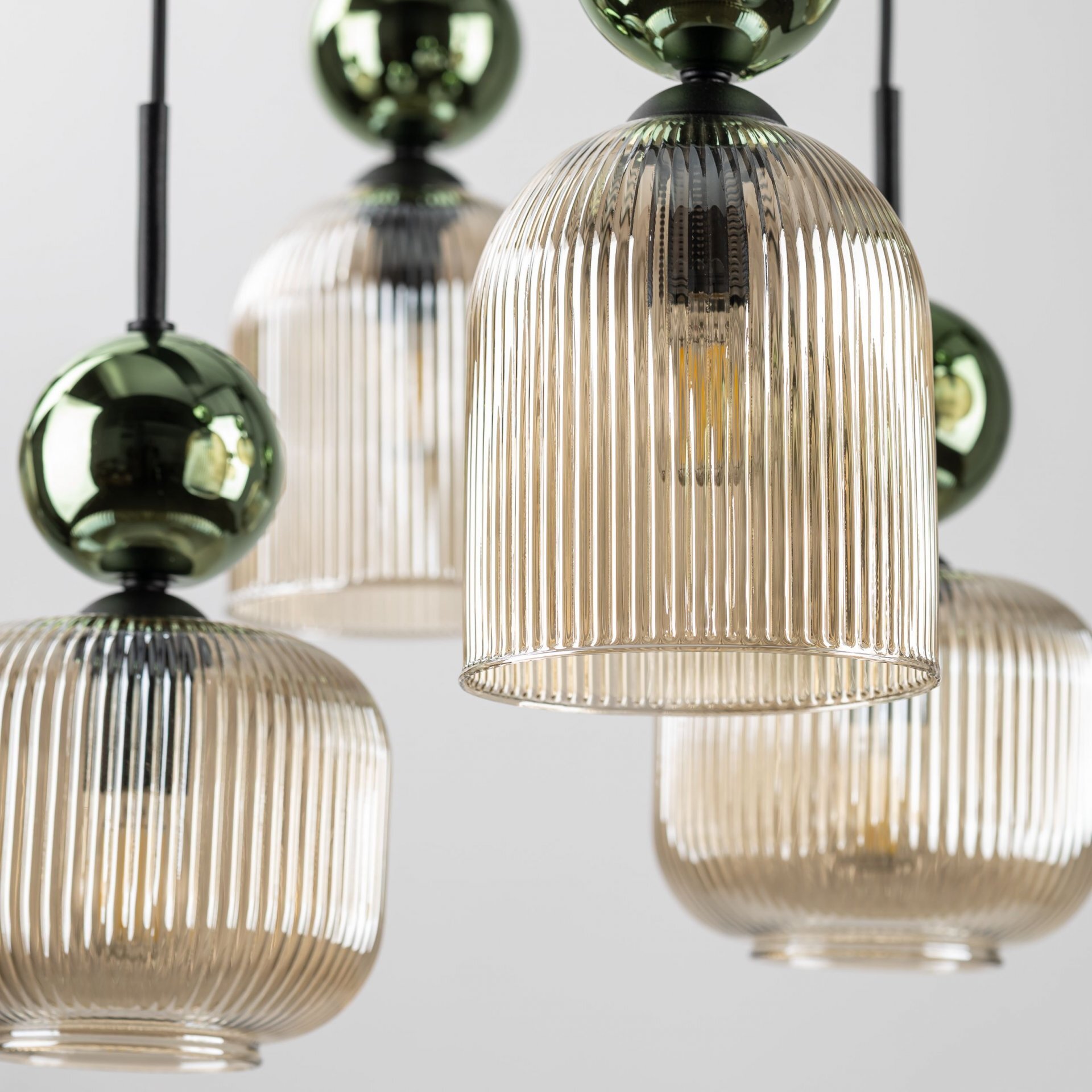 Zdjęcie przedstawia kilka wiszących lamp z żebrowanymi, przezroczystymi kloszami w kolorze bursztynowym i zielonymi elementami dekoracyjnymi. Lampy mają czarną konstrukcję i są zawieszone na czarnych przewodach.