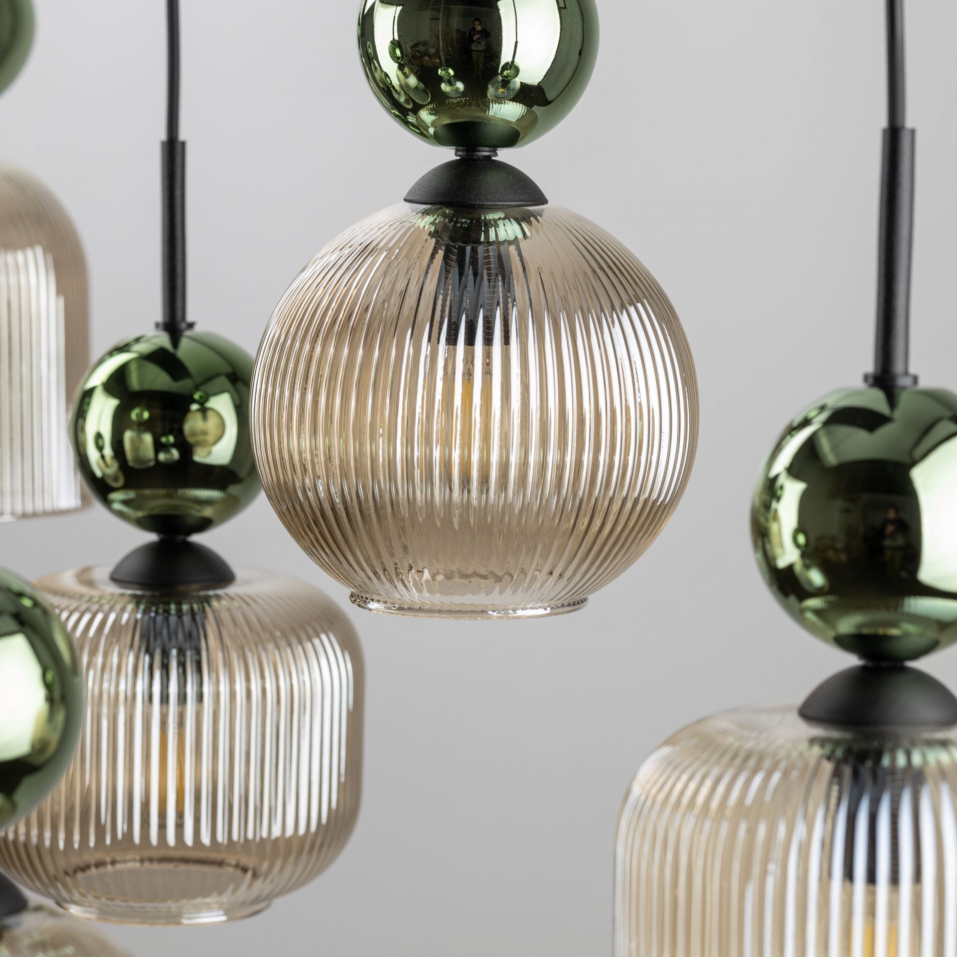 Zdjęcie przedstawia zbliżenie na lampę wiszącą z żarówkami w szklanych, żłobionych kloszach w kolorze bursztynowym. Elementy dekoracyjne lampy są w kolorze zielonym o metalicznym połysku.
