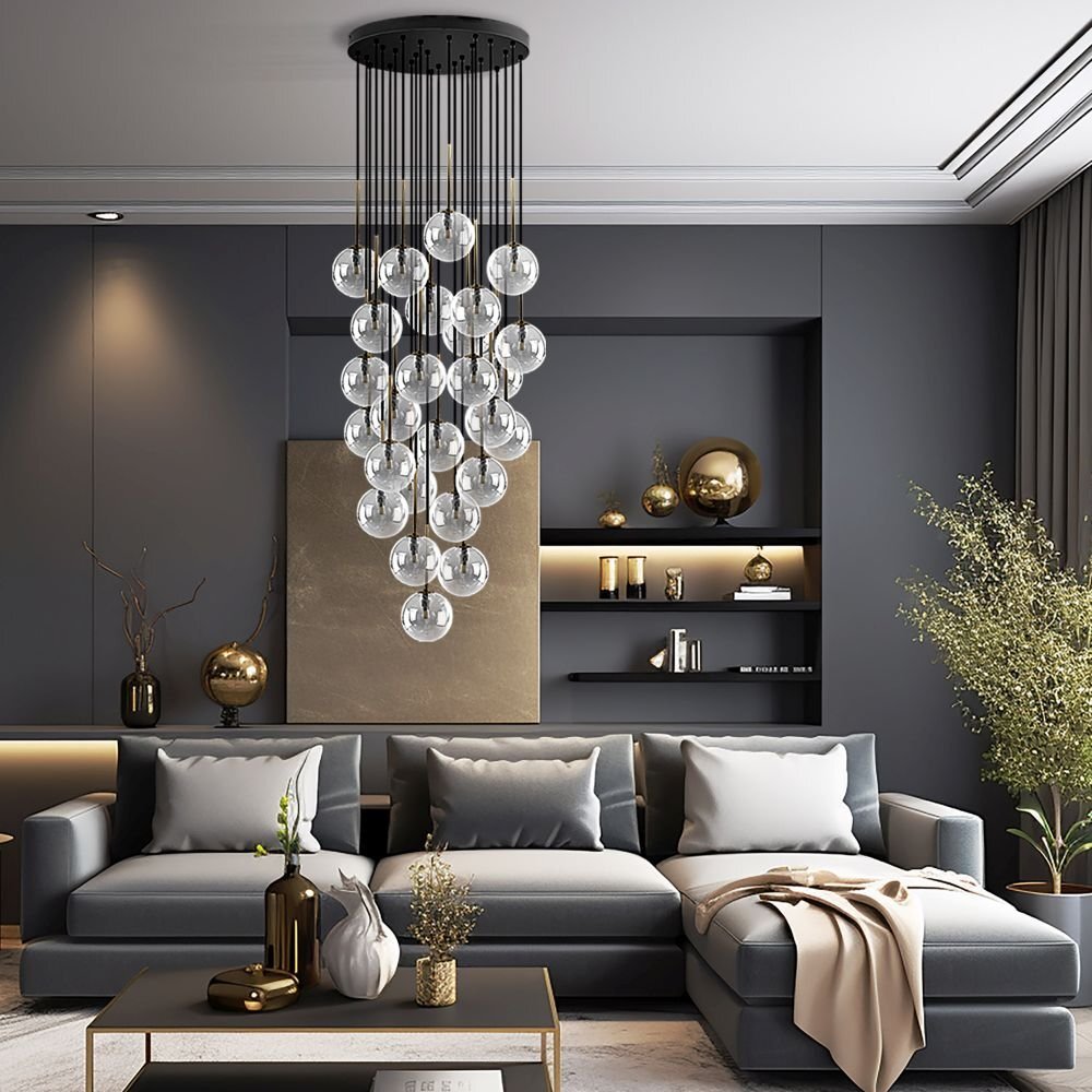 W eleganckim salonie znajduje się nowoczesna lampa wisząca z wieloma szklanymi kulami, zawieszona nad szarym narożnikiem. W tle widać ciemne półki z dekoracjami i rośliny w wazonach.