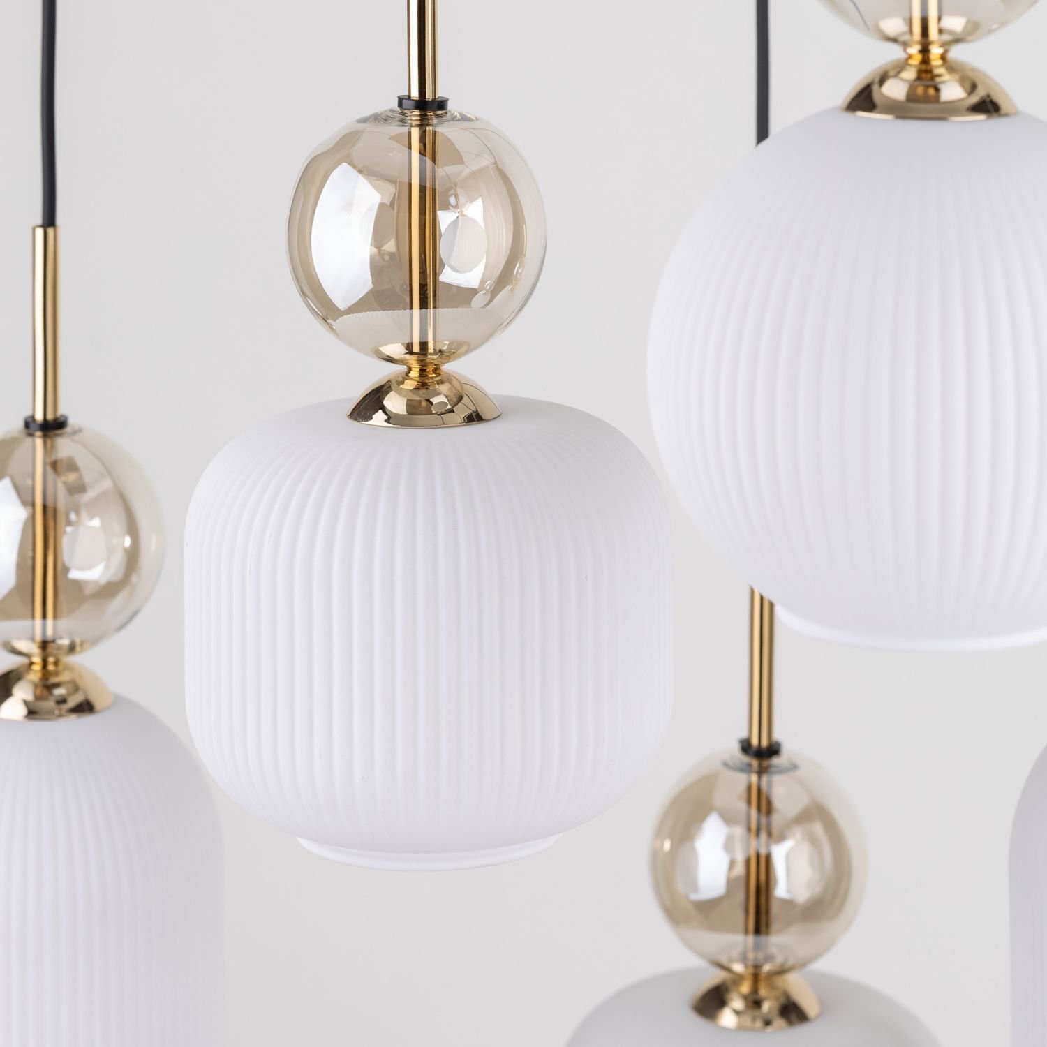 Zdjęcie przedstawia zbliżenie na elementy lampy wiszącej z białymi, żebrowanymi kloszami i złotymi detalami. Klosze są połączone z przezroczystymi, kulistymi elementami o złotym odcieniu.