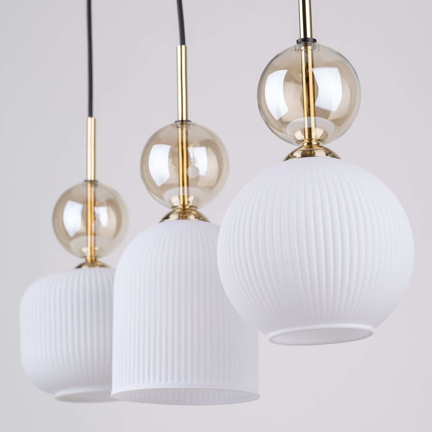 Trzy wiszące lampy z białymi, żebrowanymi kloszami i złotymi elementami. Każda lampa ma przezroczystą, kulistą ozdobę nad kloszem.