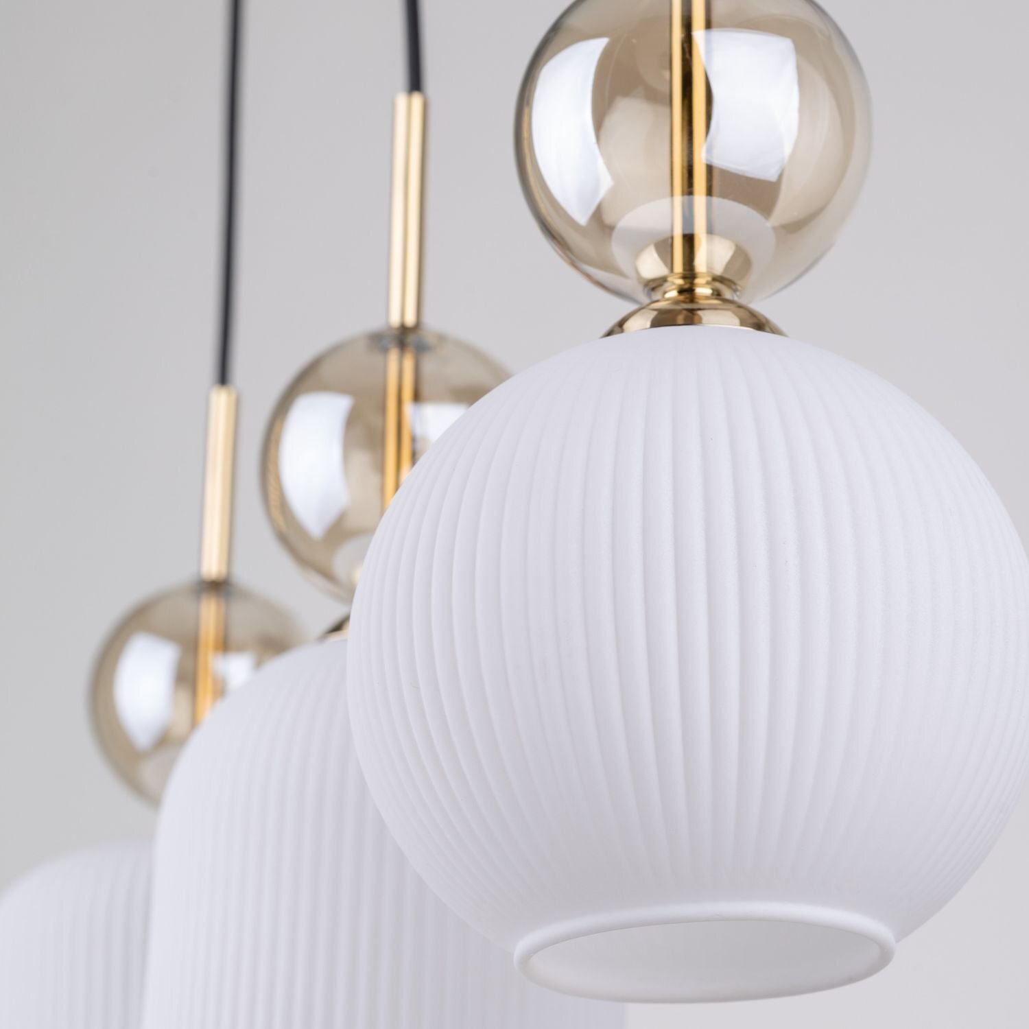 Zdjęcie przedstawia zbliżenie na lampę wiszącą z białymi, żebrowanymi kloszami i złotymi elementami dekoracyjnymi. Lampa ma nowoczesny design z kulistymi detalami.