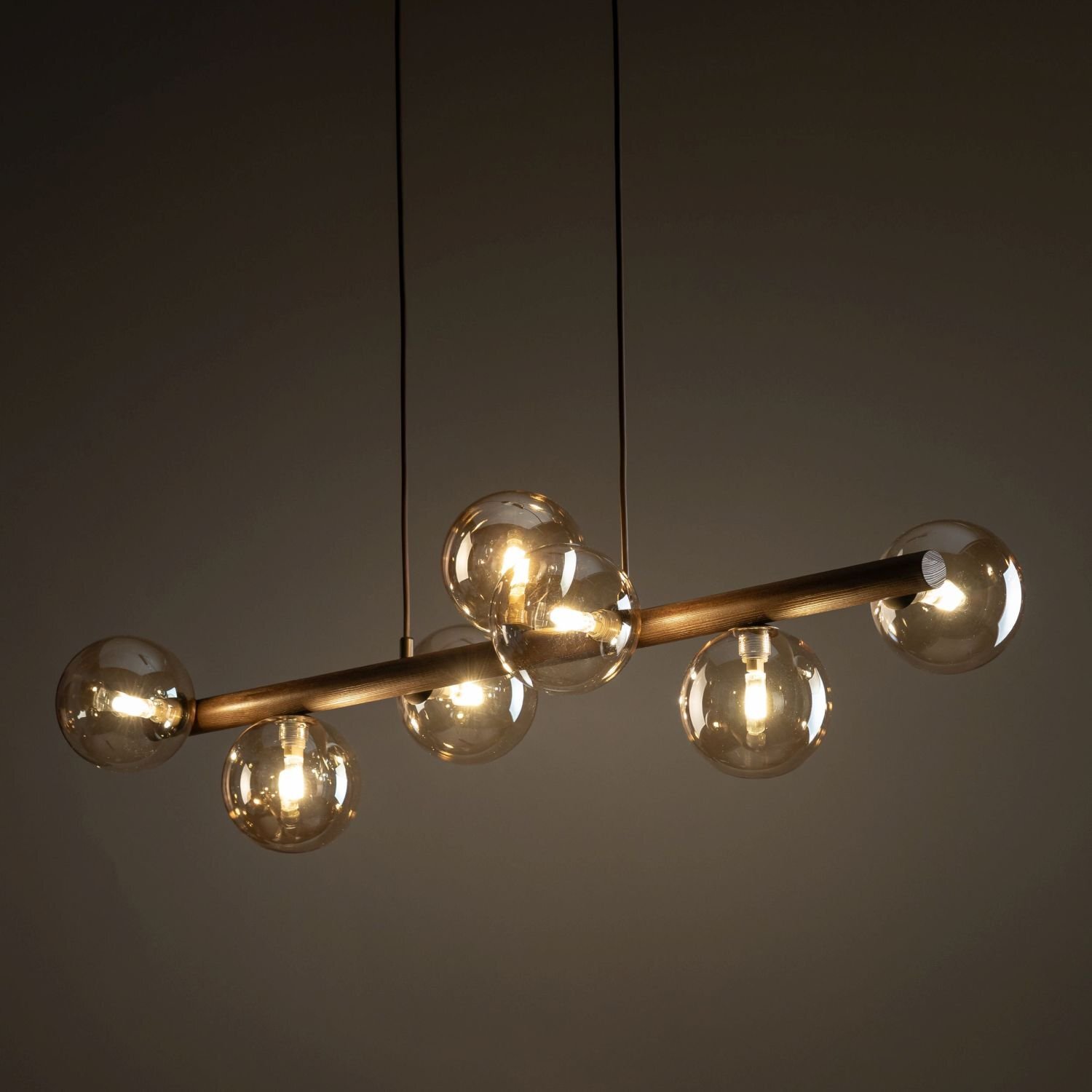 Lampa wisząca z siedmioma bursztynowymi szklanymi kloszami na metalowo-drewnianej konstrukcji. Światło emituje ciepły blask, tworząc elegancki efekt wizualny.