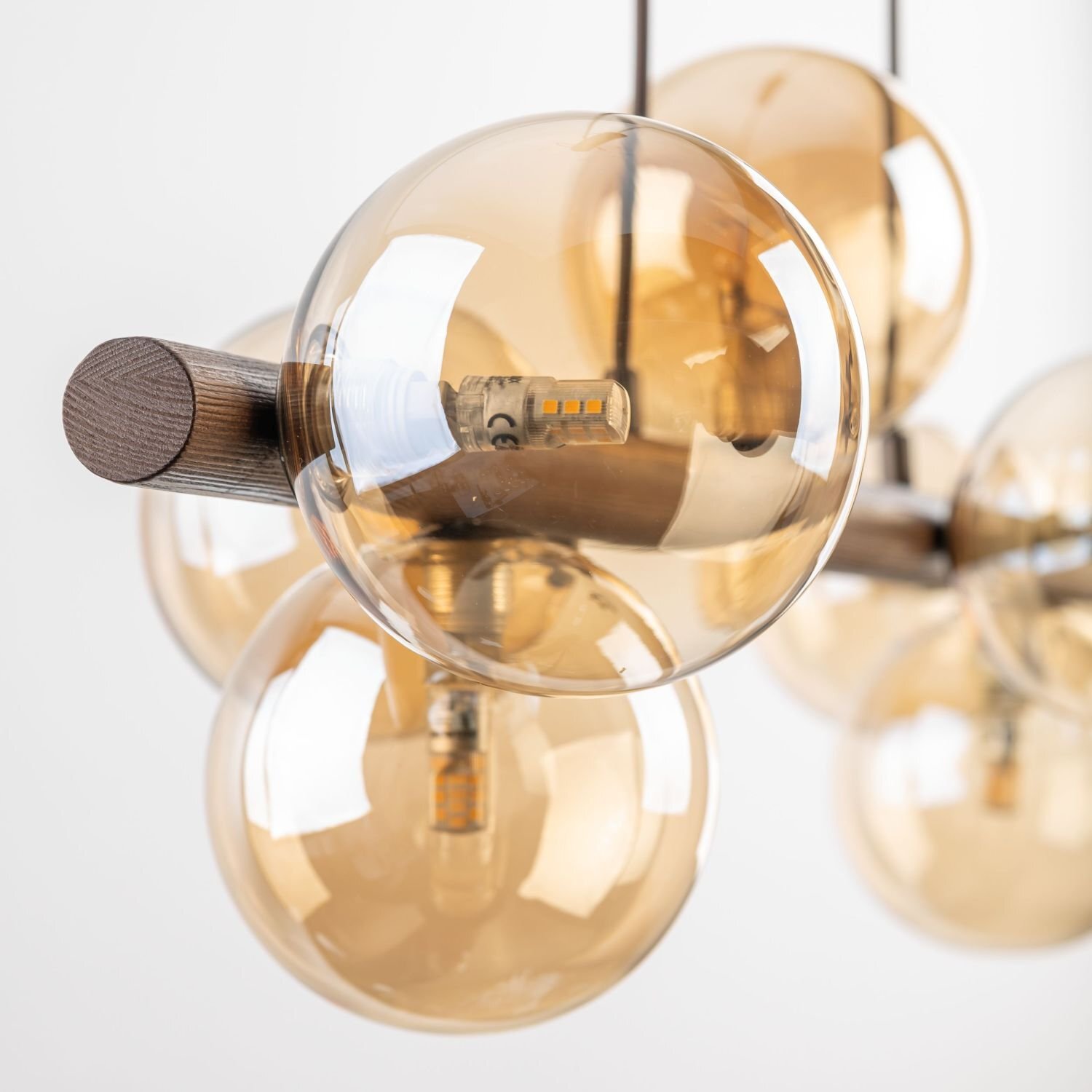 Lampa wisząca z bursztynowymi szklanymi kloszami i elementami z drewna oraz metalu. Wewnątrz kloszy widoczne są żarówki LED.
