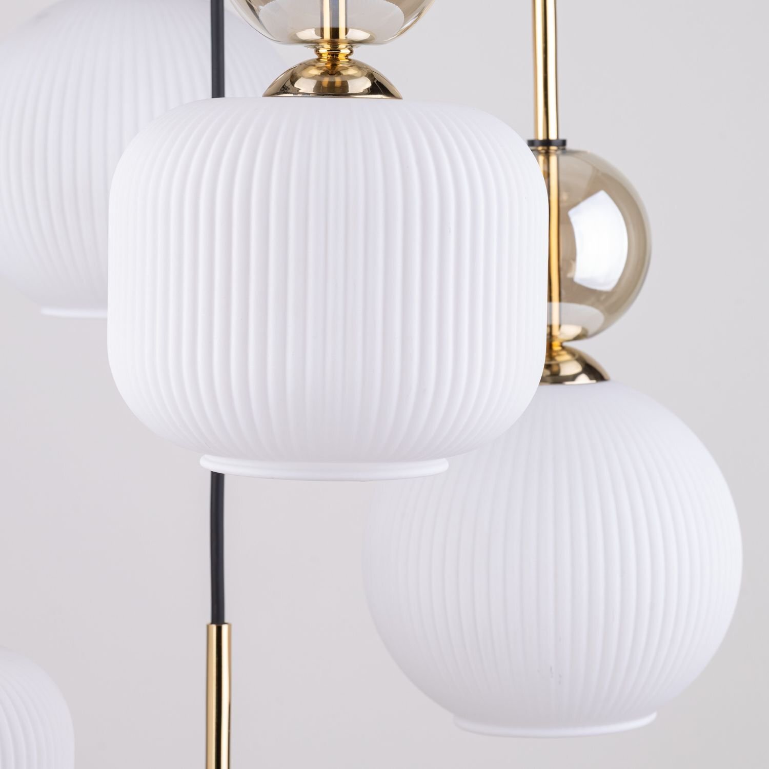 Na obrazie widoczne są białe, żebrowane klosze lampy wiszącej z elementami w kolorze złotym. Lampa ma elegancki, nowoczesny design.