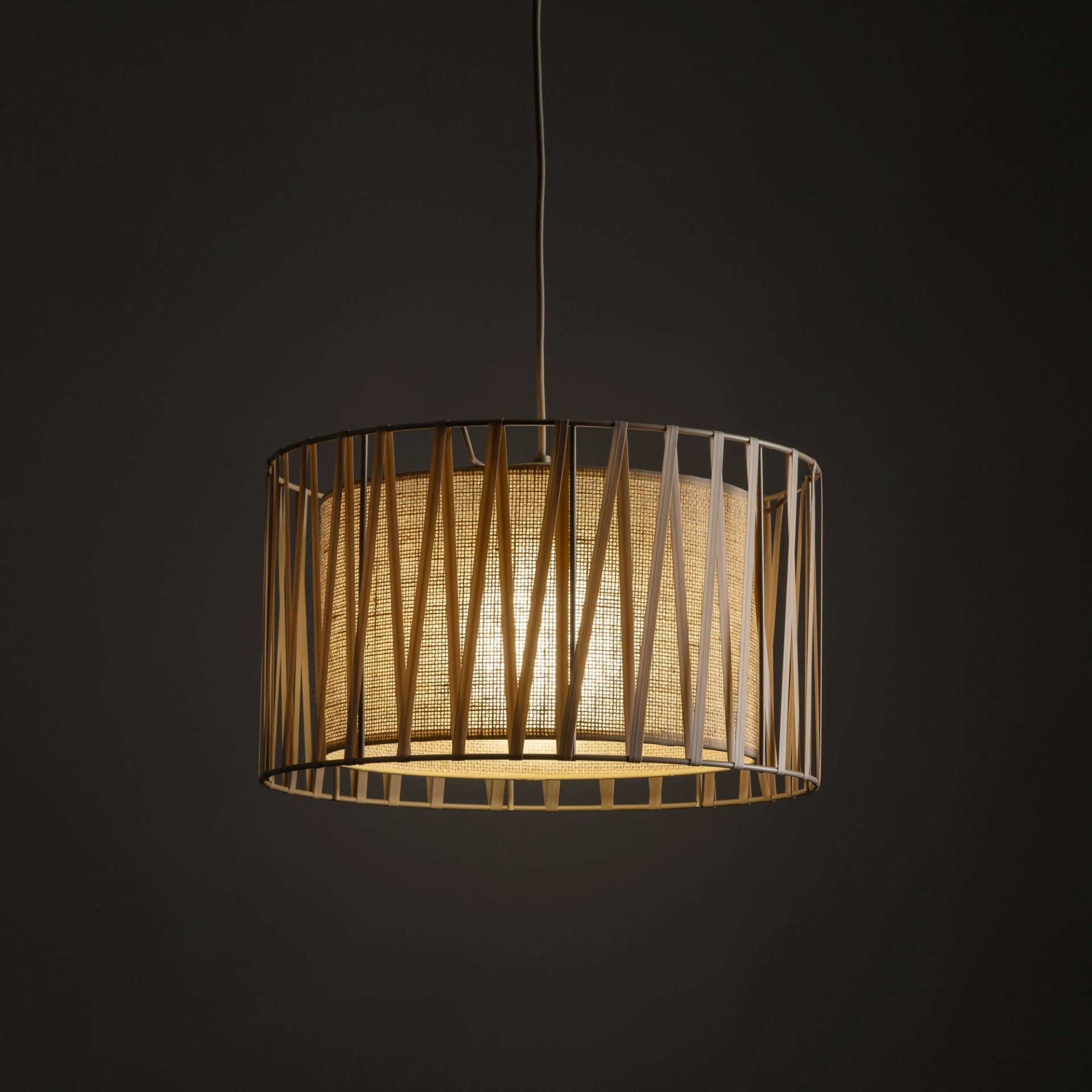 Lampa wisząca z beżowym abażurem z juty, otoczona metalową ramą o geometrycznym wzorze. Światło jest ciepłe i przytulne, tworząc przyjemną atmosferę.