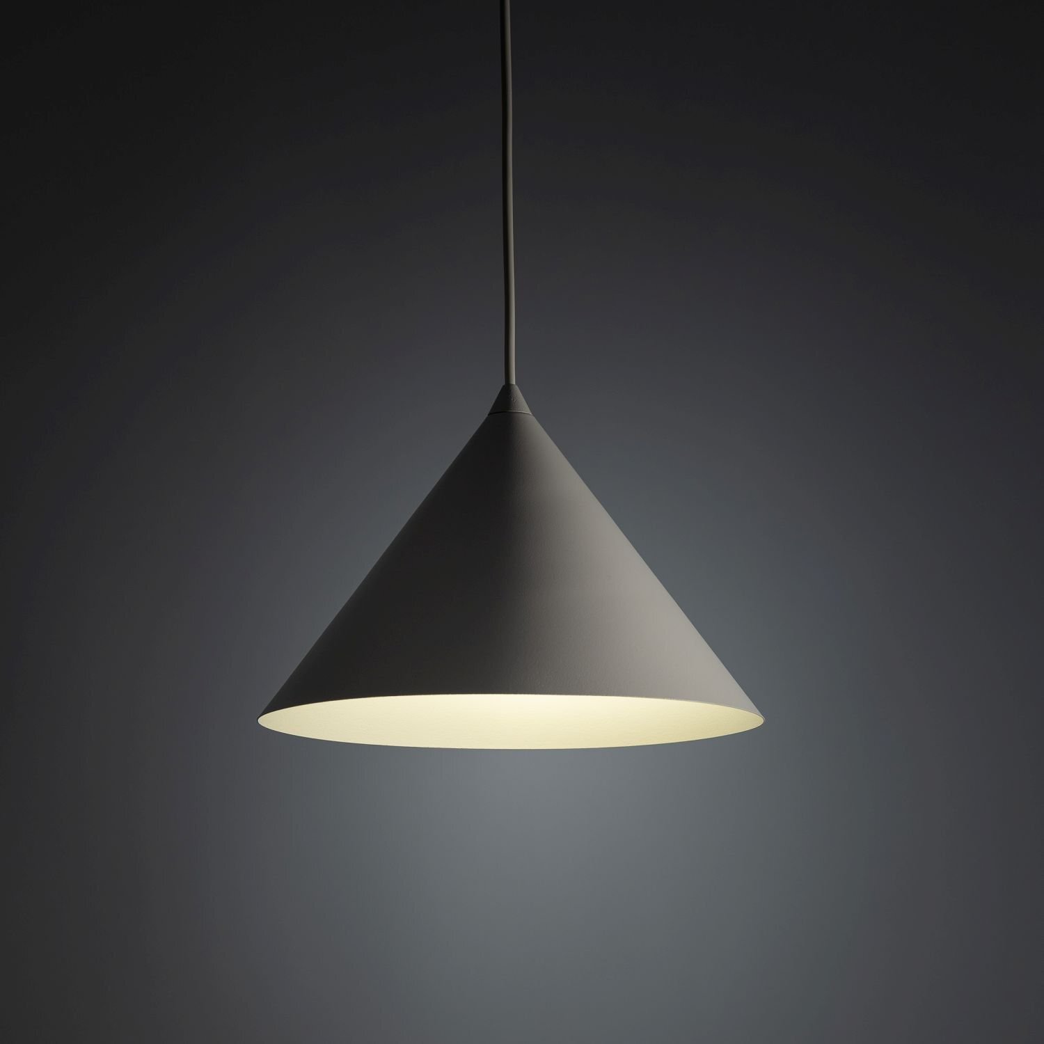 Na obrazie widoczna jest lampa wisząca o stożkowym kształcie, emitująca jasne światło. Tło jest ciemne, co podkreśla kontrast z oświetleniem lampy.