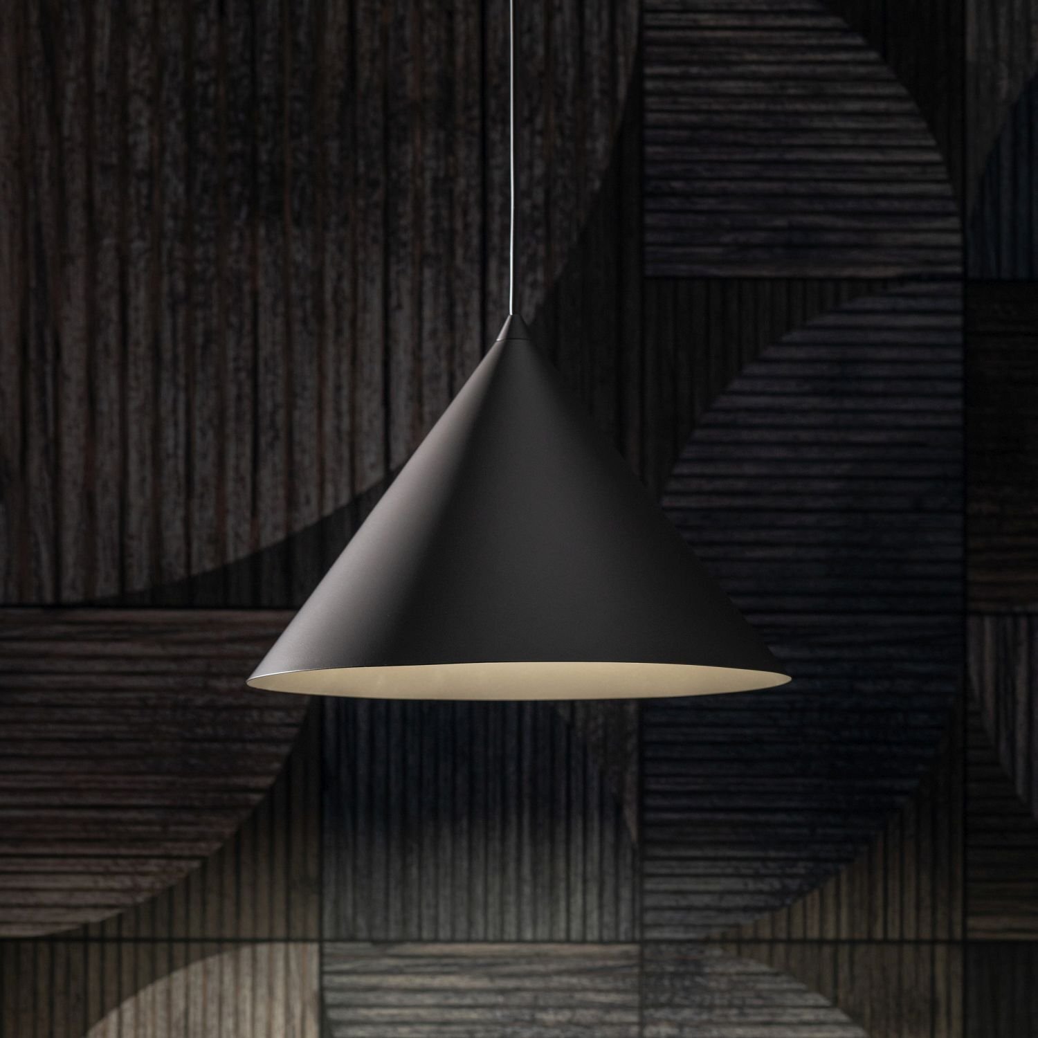 Na obrazie widoczna jest lampa wisząca w kształcie stożka, w kolorze ciemnobrązowym. Tło stanowi ciemna, geometryczna ściana z drewnianymi panelami.