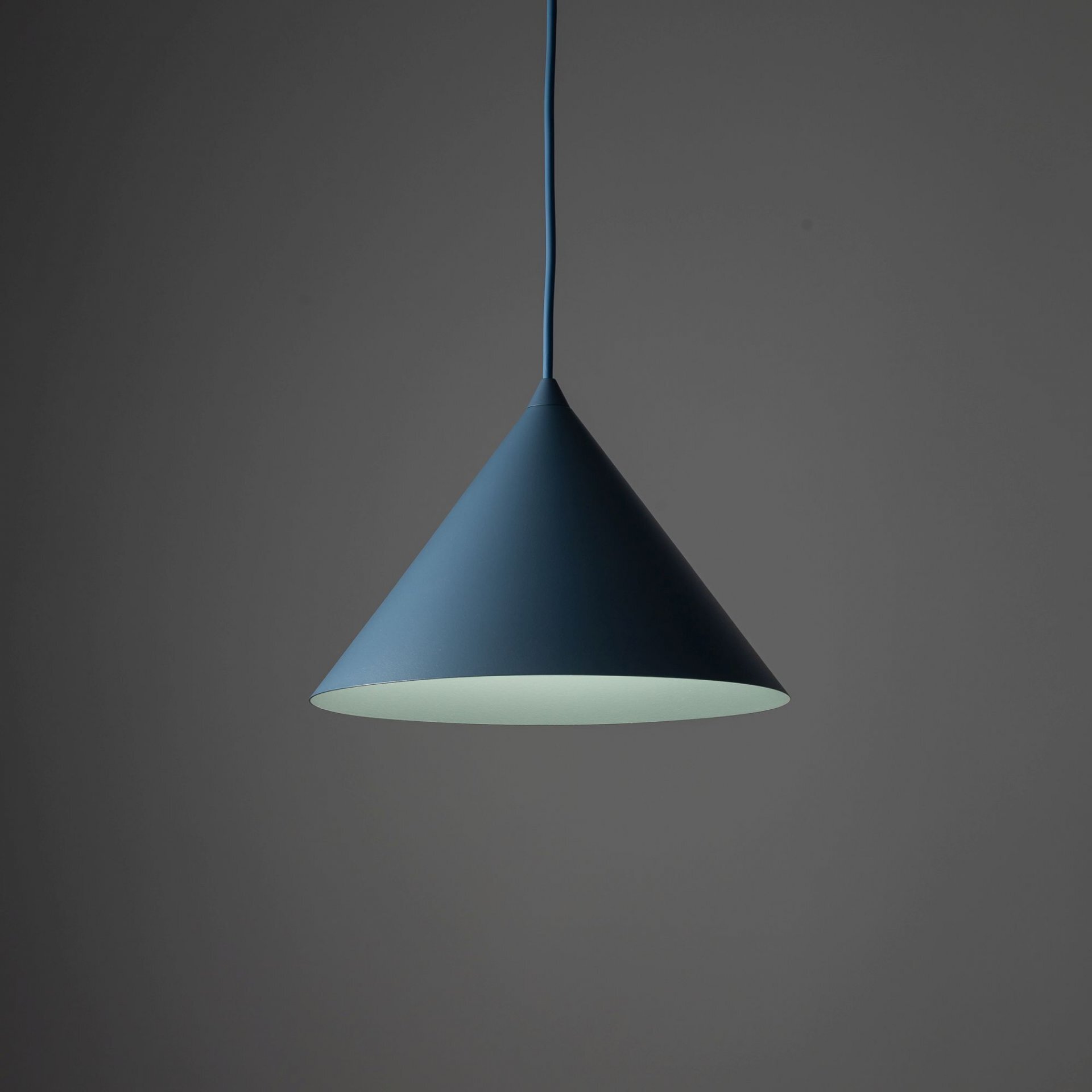 Na obrazie widoczna jest granatowa, stożkowa lampa wisząca z regulowanym przewodem. Tło jest jednolite i ciemnoszare.