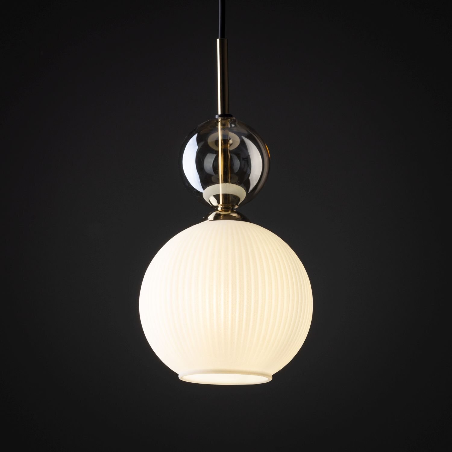 Lampa wisząca z białym, żebrowanym kloszem i złotymi elementami, zawieszona na czarnym przewodzie. W tle ciemne tło, które podkreśla elegancki design lampy.