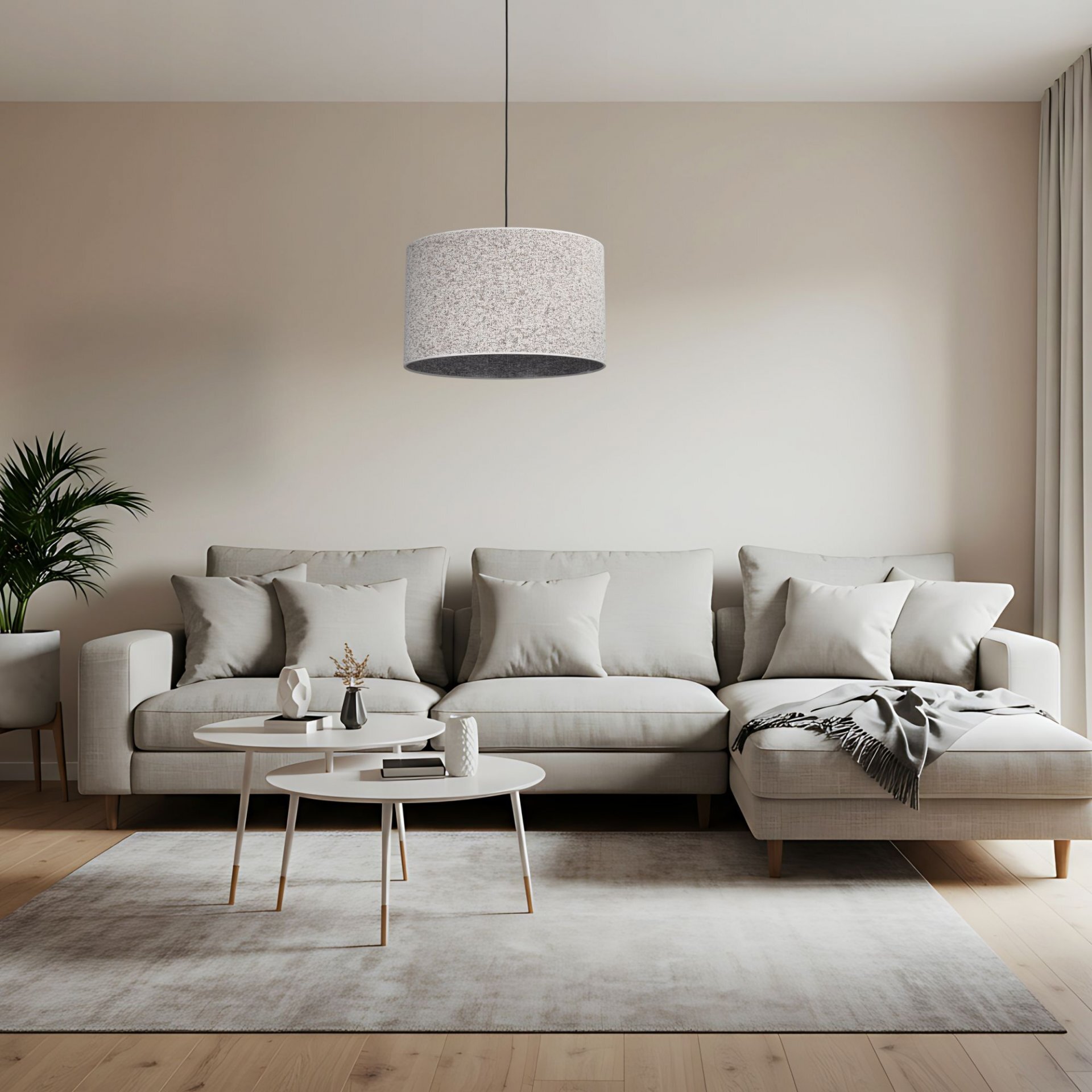 W nowoczesnym salonie znajduje się szara sofa z poduszkami, przed którą stoją dwa okrągłe stoliki. Nad sofą wisi lampa z dużym, cylindrycznym kloszem w jasnym kolorze.