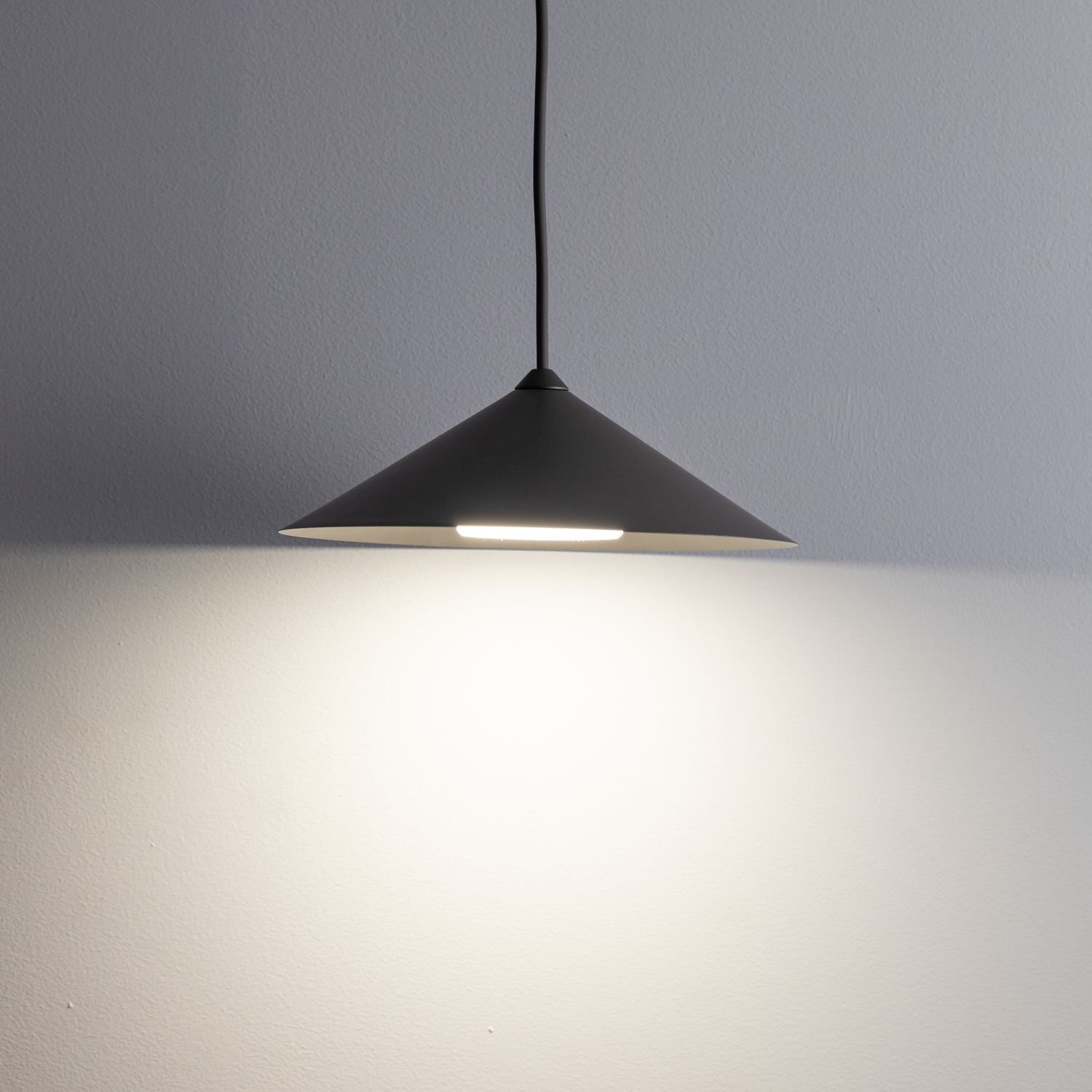 Brązowa, stalowa lampa wisząca o stożkowym kształcie, emitująca światło na ścianę. Lampa zawieszona jest na czarnym przewodzie.